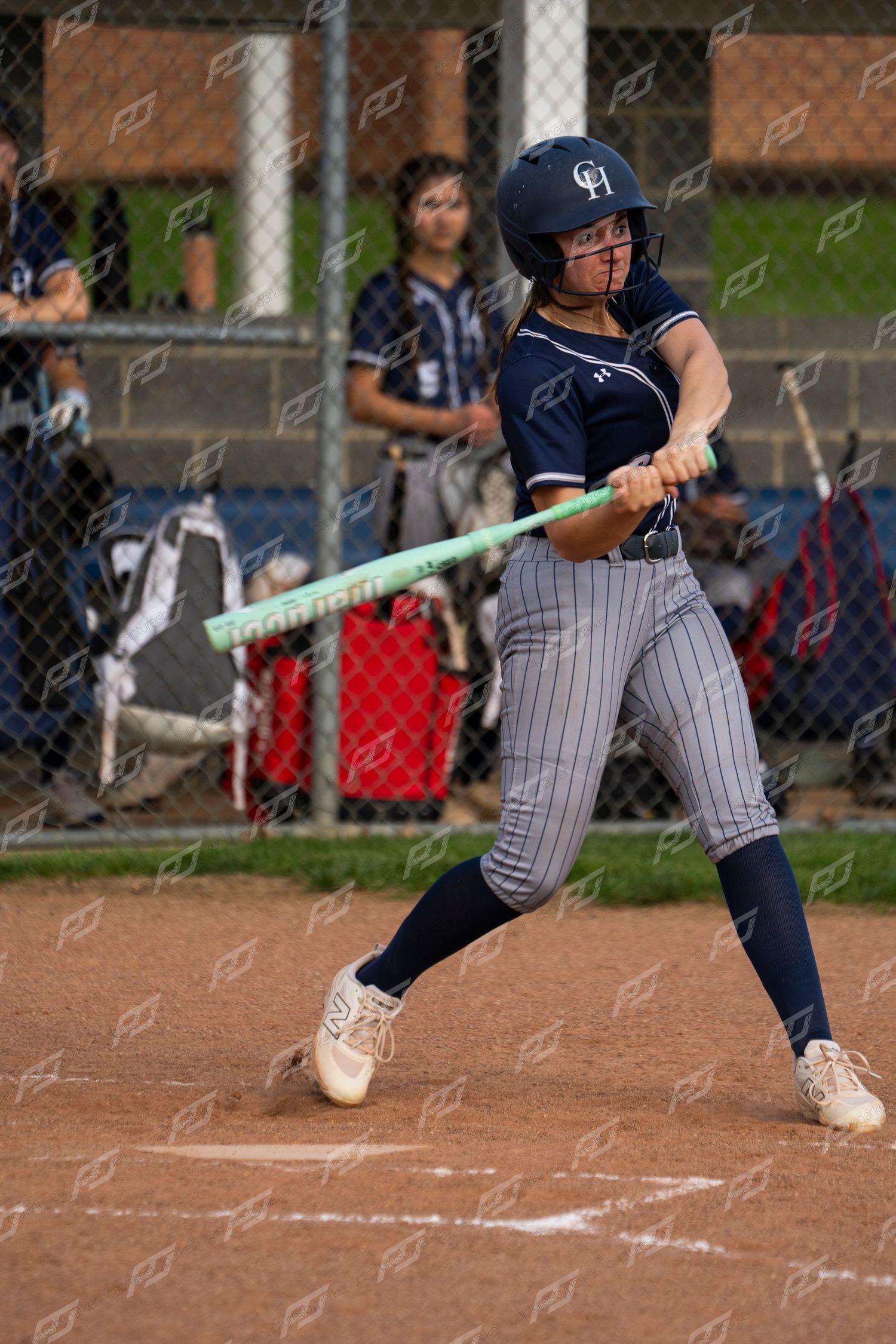 Female softball player in navy helmet and pinstripe uniform swings at pitch.