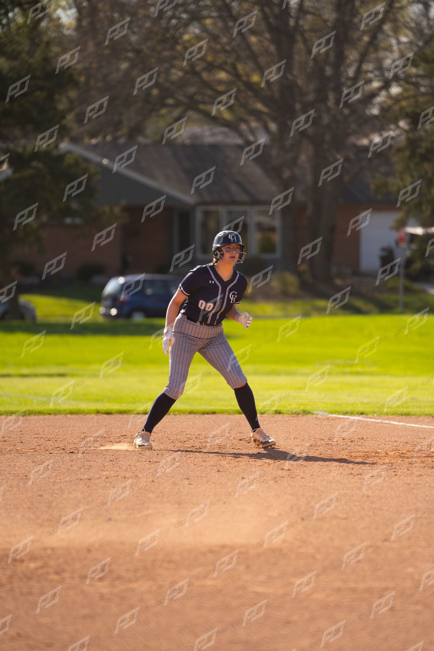 Female softball player in navy pinstripe uniform takes a lead off base during an outdoor game.