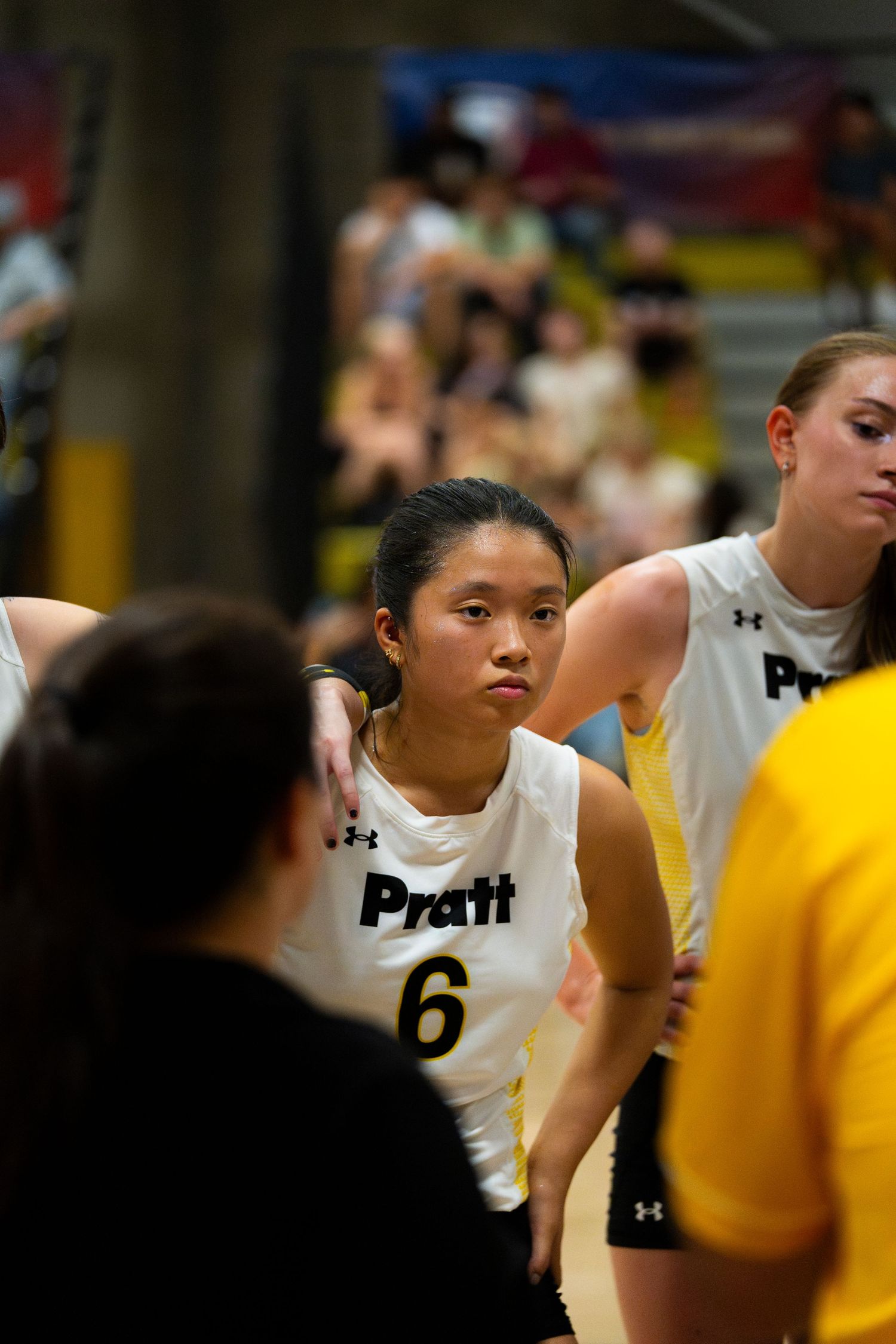 Pratt women's basketball player number 6 listens intently during a timeout huddle on the court.