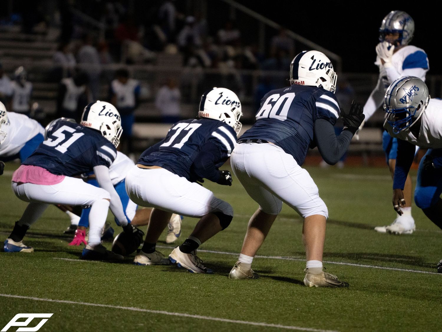 Camp Hill Lions offensive linemen numbers 51, 71, and 60 line up at scrimmage during a night game.