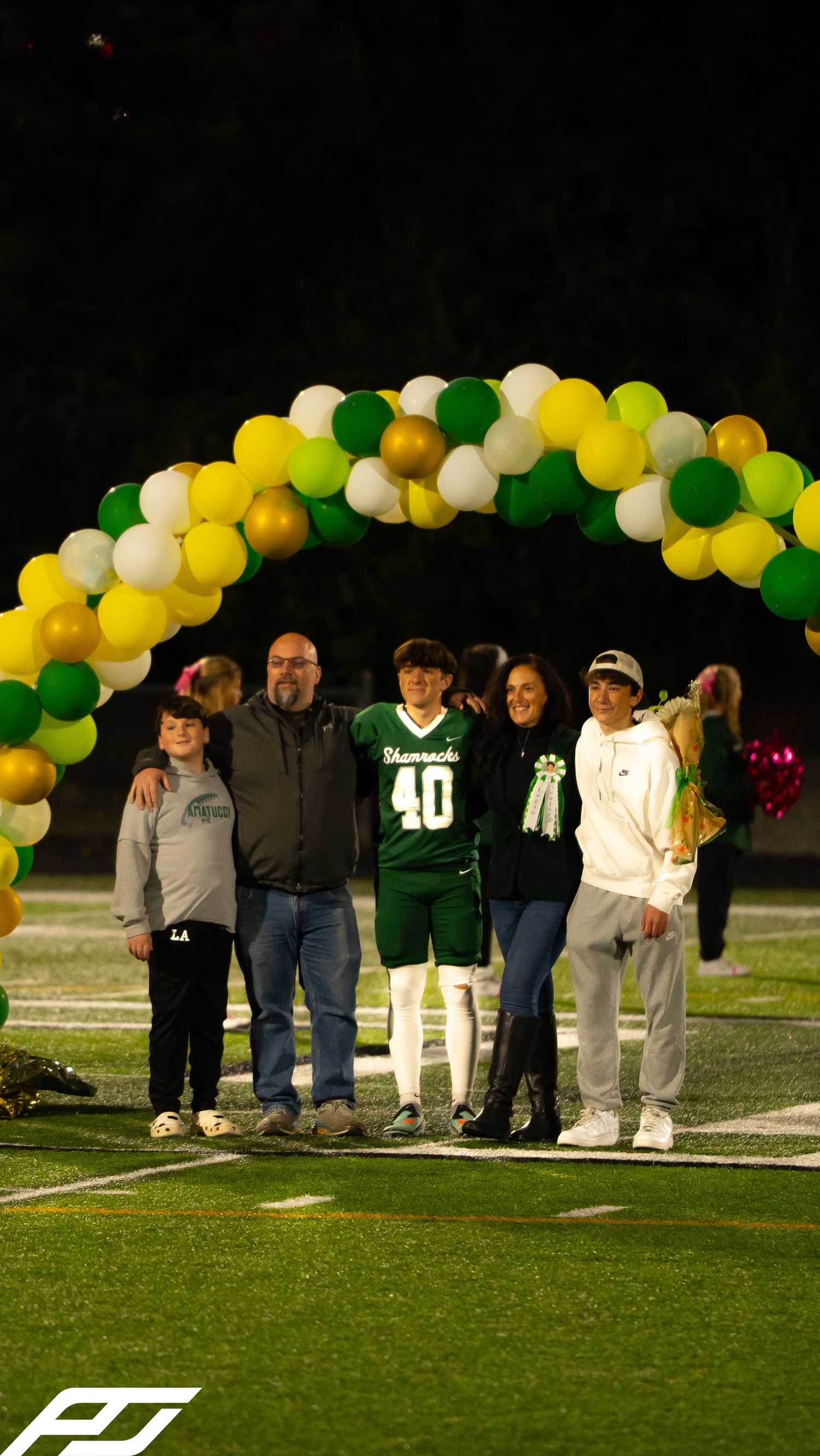 Shamrocks football player #40 celebrates senior night with family under green, gold, and white balloon arch.
