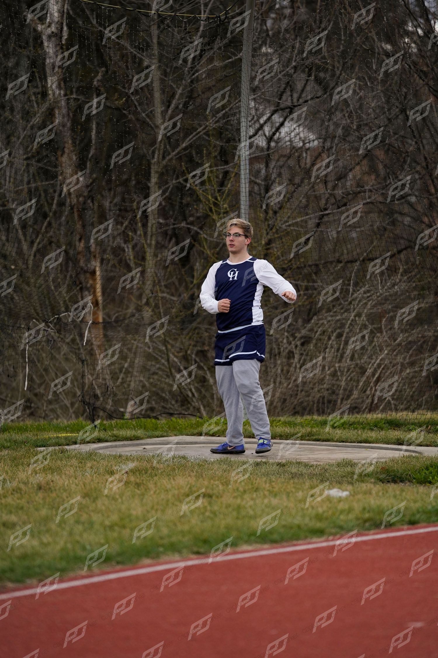 Male athlete in navy uniform preparing to throw shot put in a grass circle area.