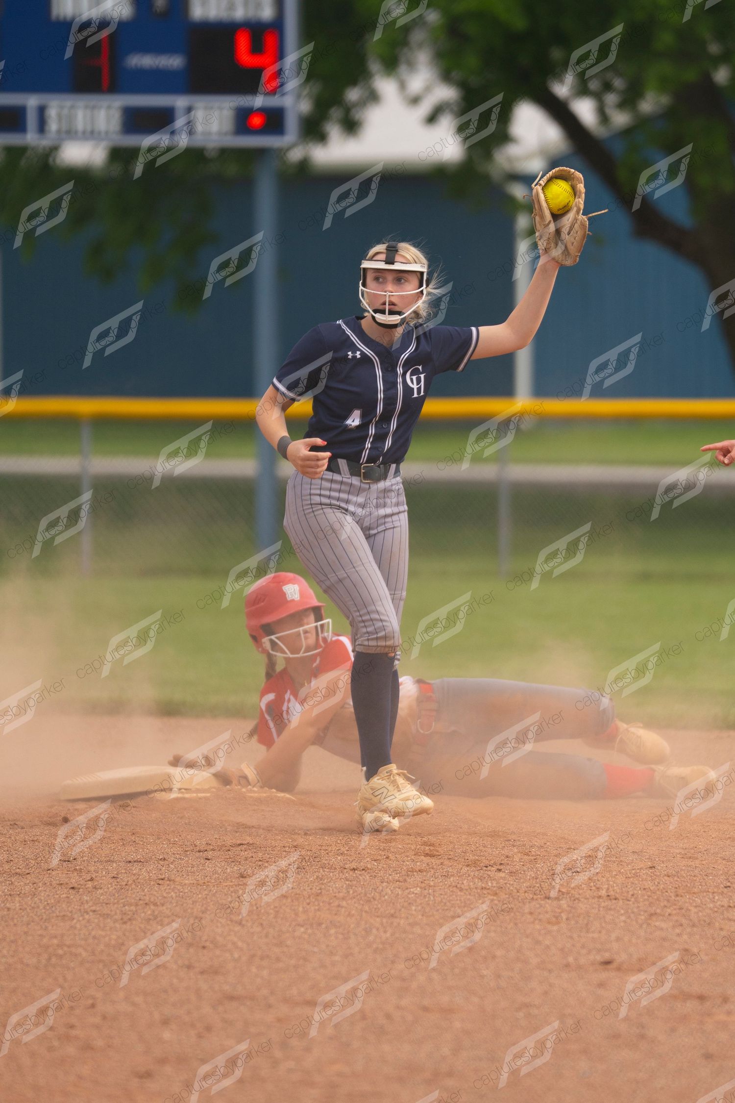 Softball infielder catches ball at second base as opposing player slides in a cloud of dust.
