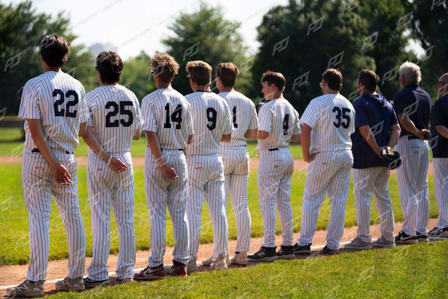 Youth baseball team in pinstripe uniforms lined up on field during pre-game ceremonies.