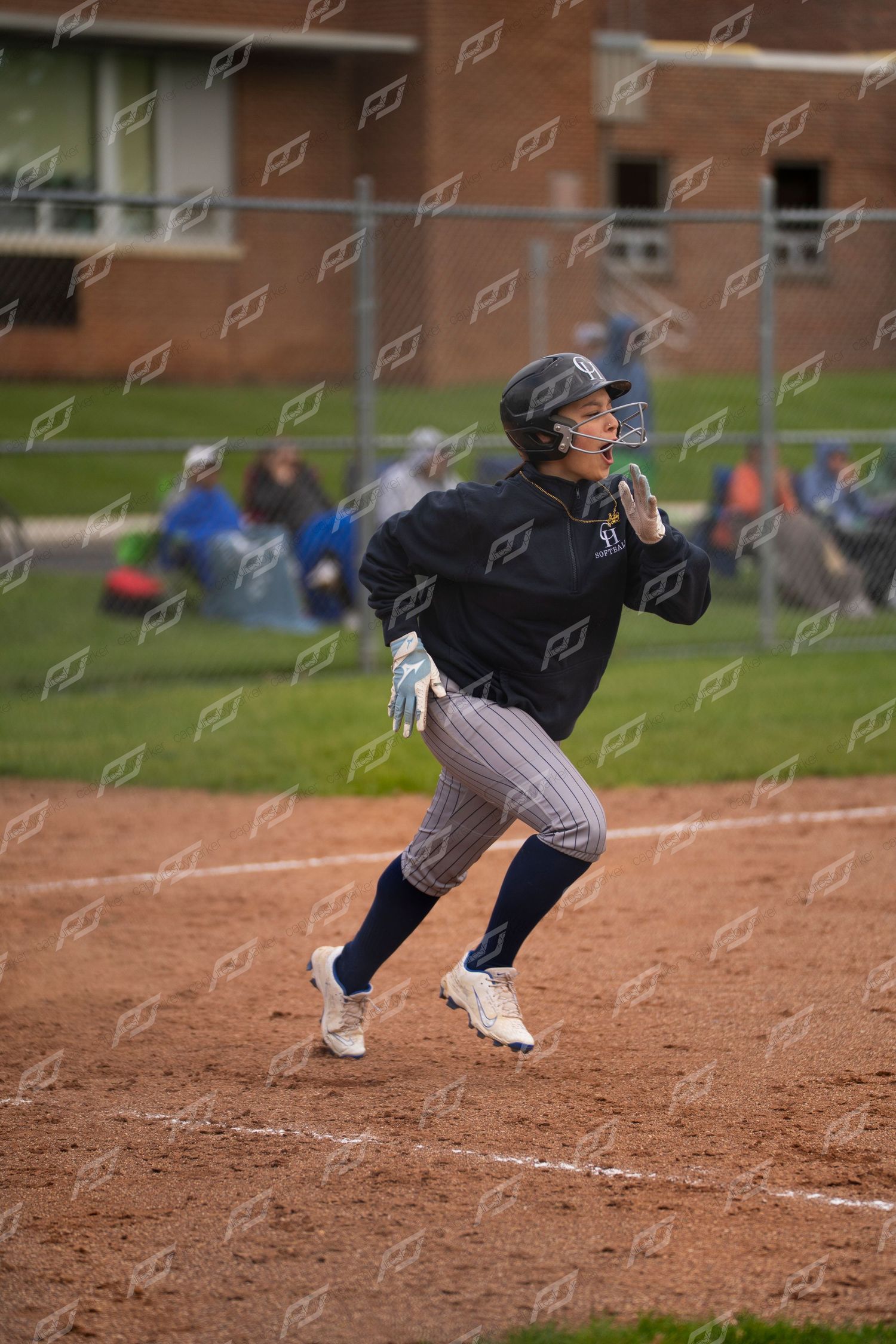 Female softball player runs bases in navy pinstripe uniform during an outdoor game.
