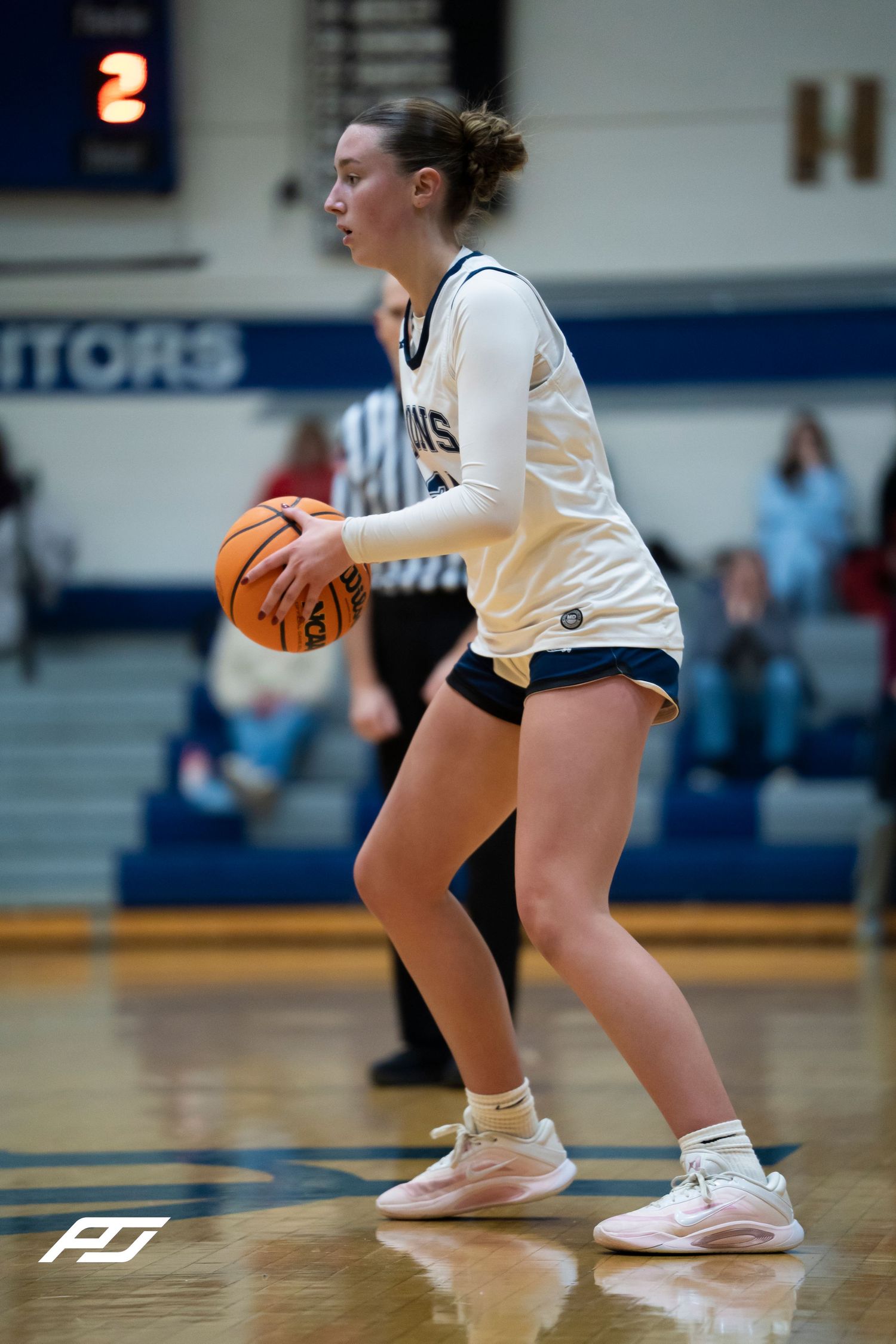 Female Lions basketball player holds the ball near the visitors section during a high school girls basketball game.