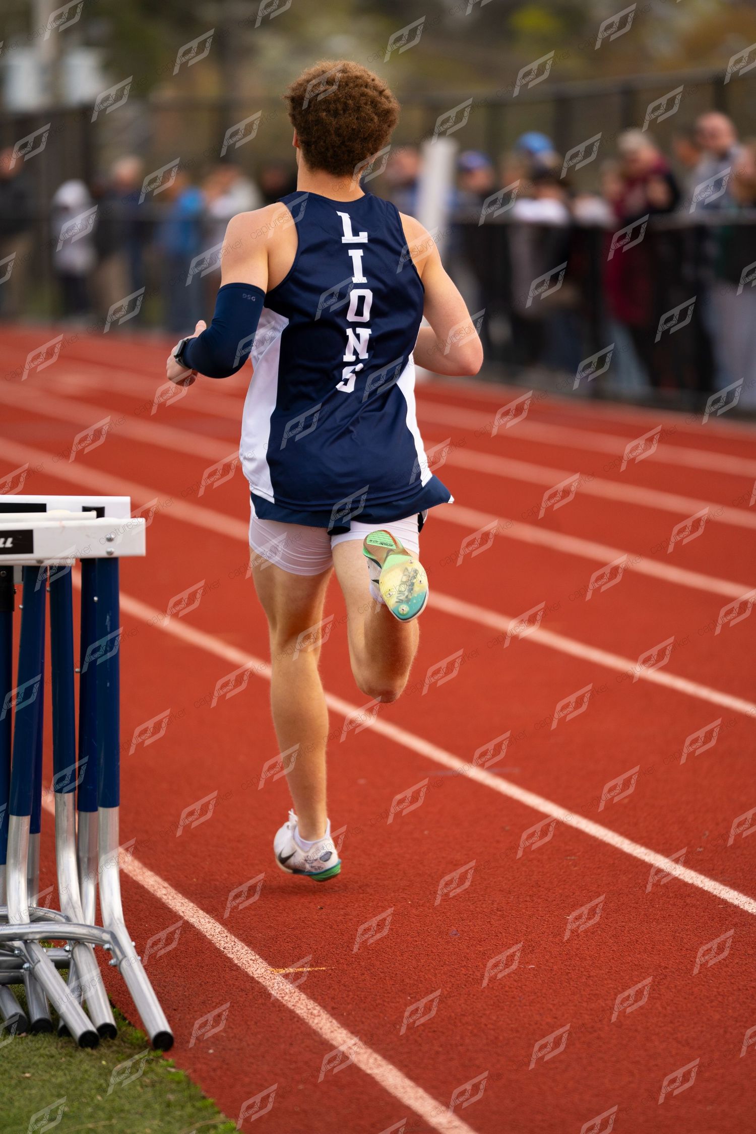 Male Lions track athlete viewed from behind running on red outdoor track.