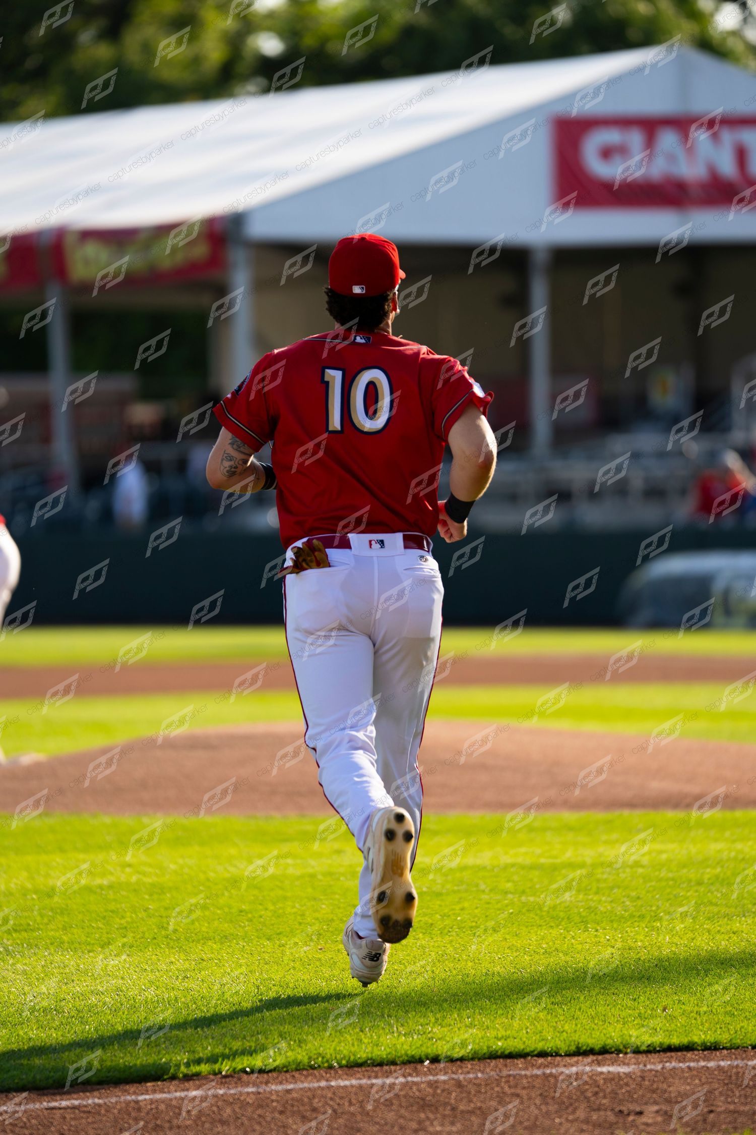 Baseball player #10 in red and white uniform running toward the dugout during an evening game.