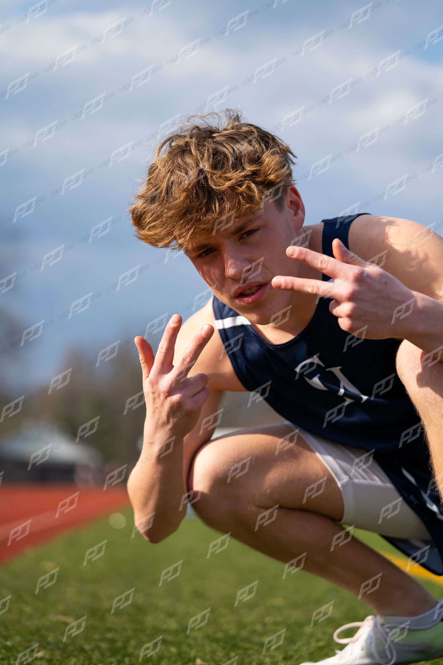 Male track athlete in navy CH uniform crouches and poses with hand gestures on track.