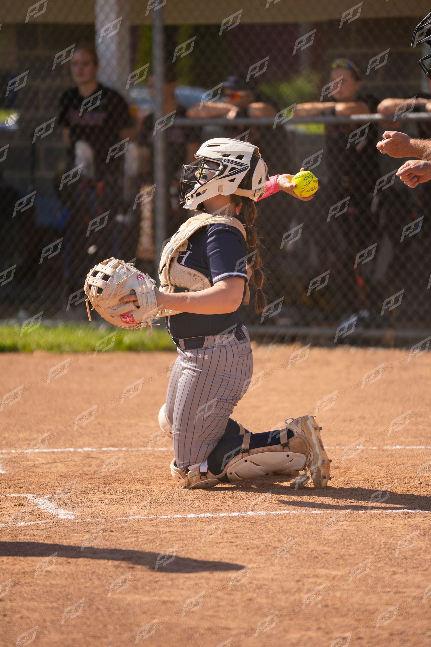 Softball catcher in full gear reaches to catch a yellow ball at home plate.
