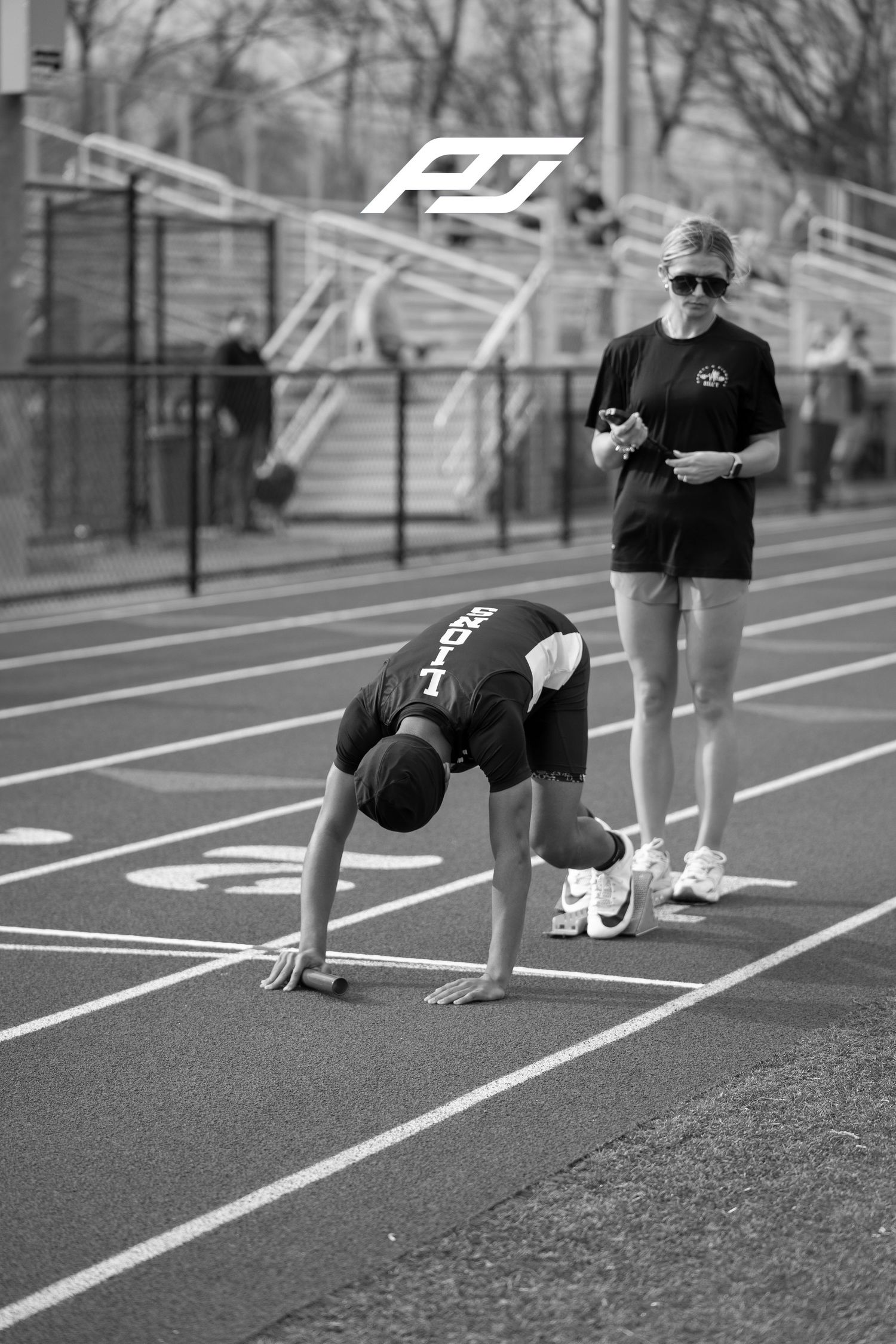 Athlete in starting position on track while coach observes during a sprint race event.