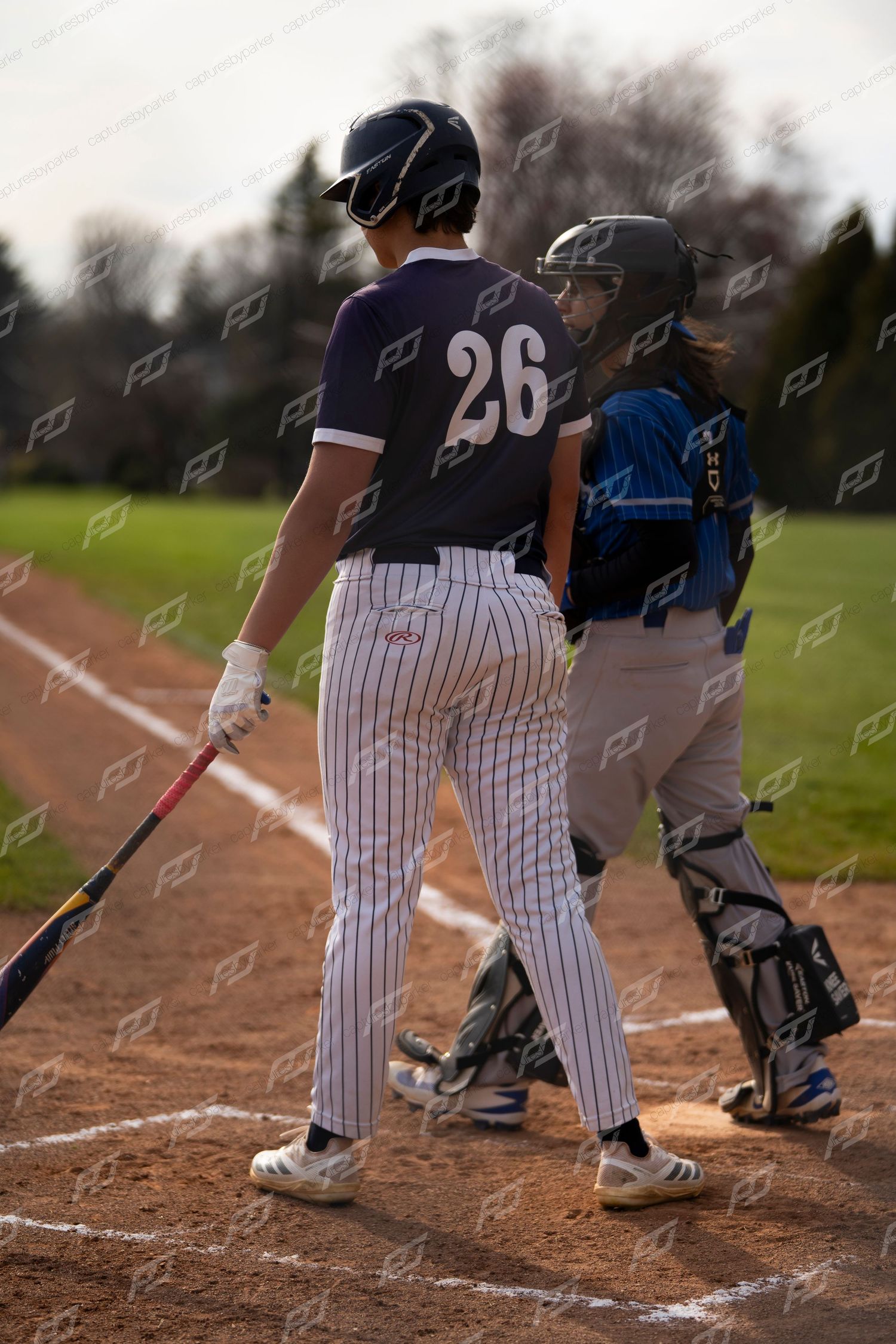 Baseball player #26 stands at home plate beside the catcher during a youth baseball game.