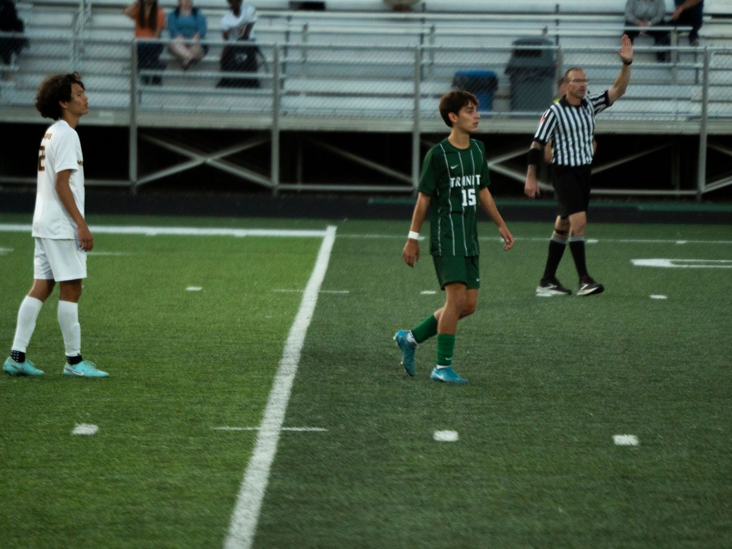 Youth soccer player number 15 in green walks near a referee during an outdoor soccer game.