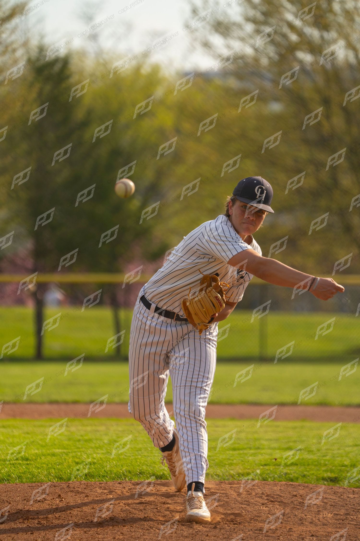 Baseball pitcher in white pinstripe uniform delivers a pitch on the mound during a game.