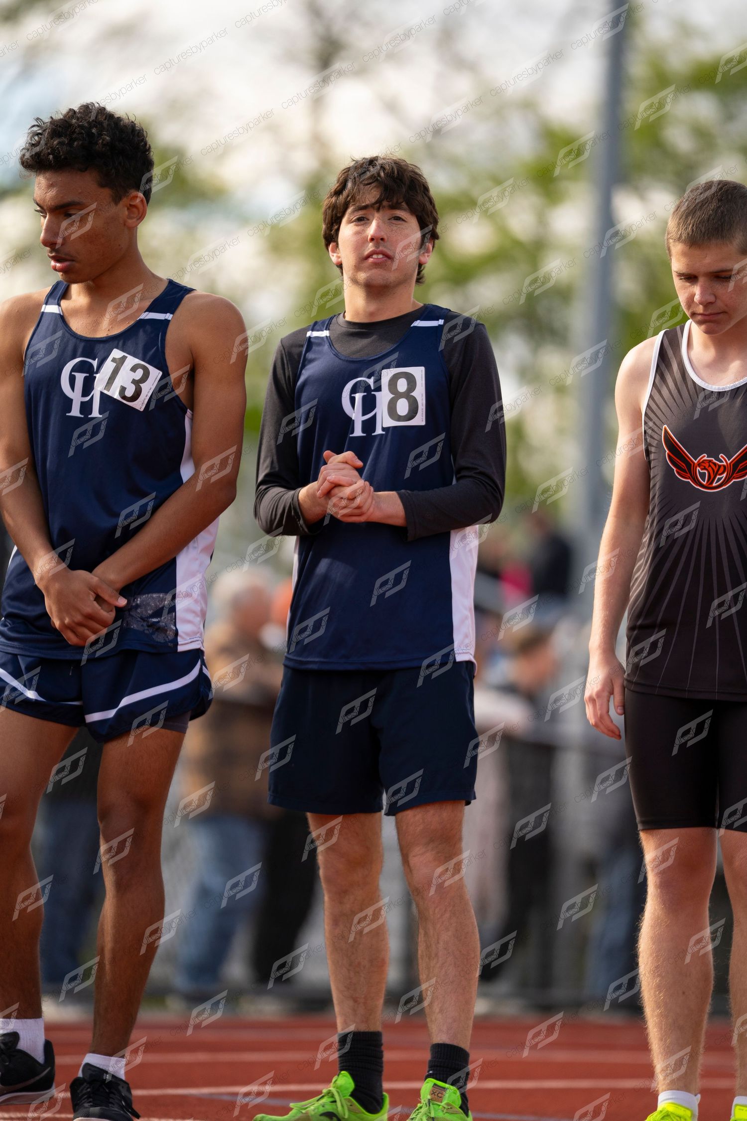 Three male track athletes stand at the starting line preparing for a race.