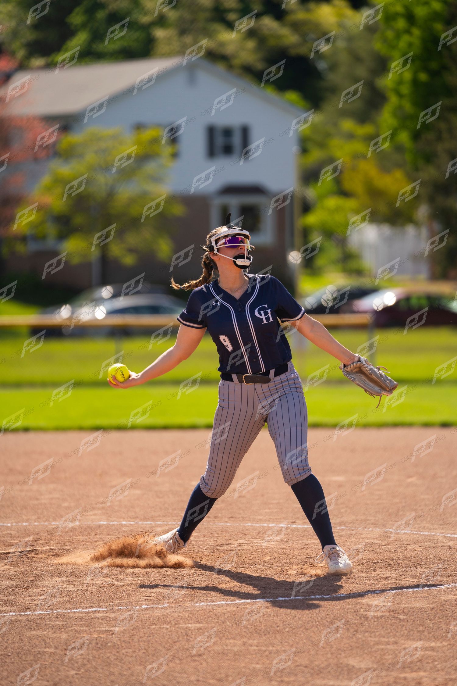Female softball pitcher releases a yellow ball during a sunny outdoor game.