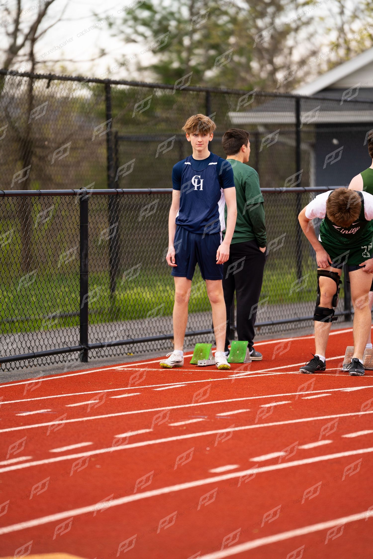 CH high school male track athlete stands at starting line on red track during outdoor meet.