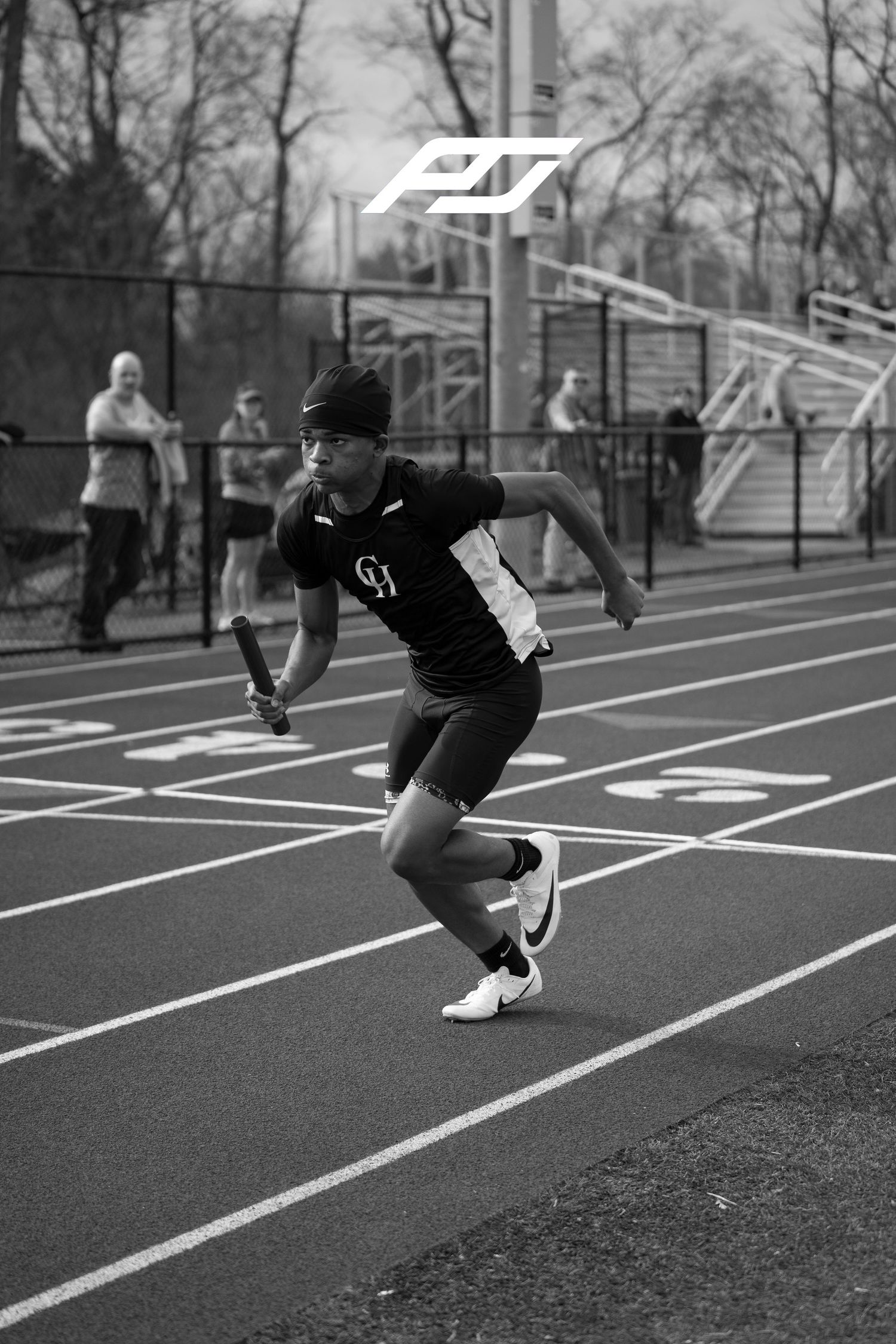 Track athlete sprints with relay baton wearing GH uniform during outdoor relay race.