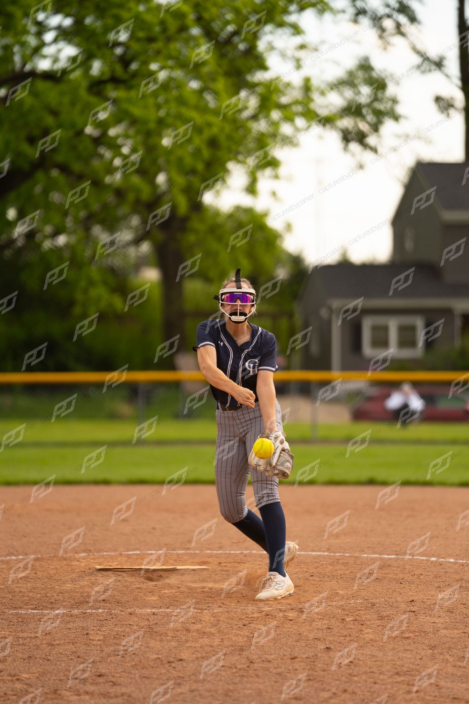 Female softball pitcher in navy pinstripe uniform delivering pitch on outdoor mound.