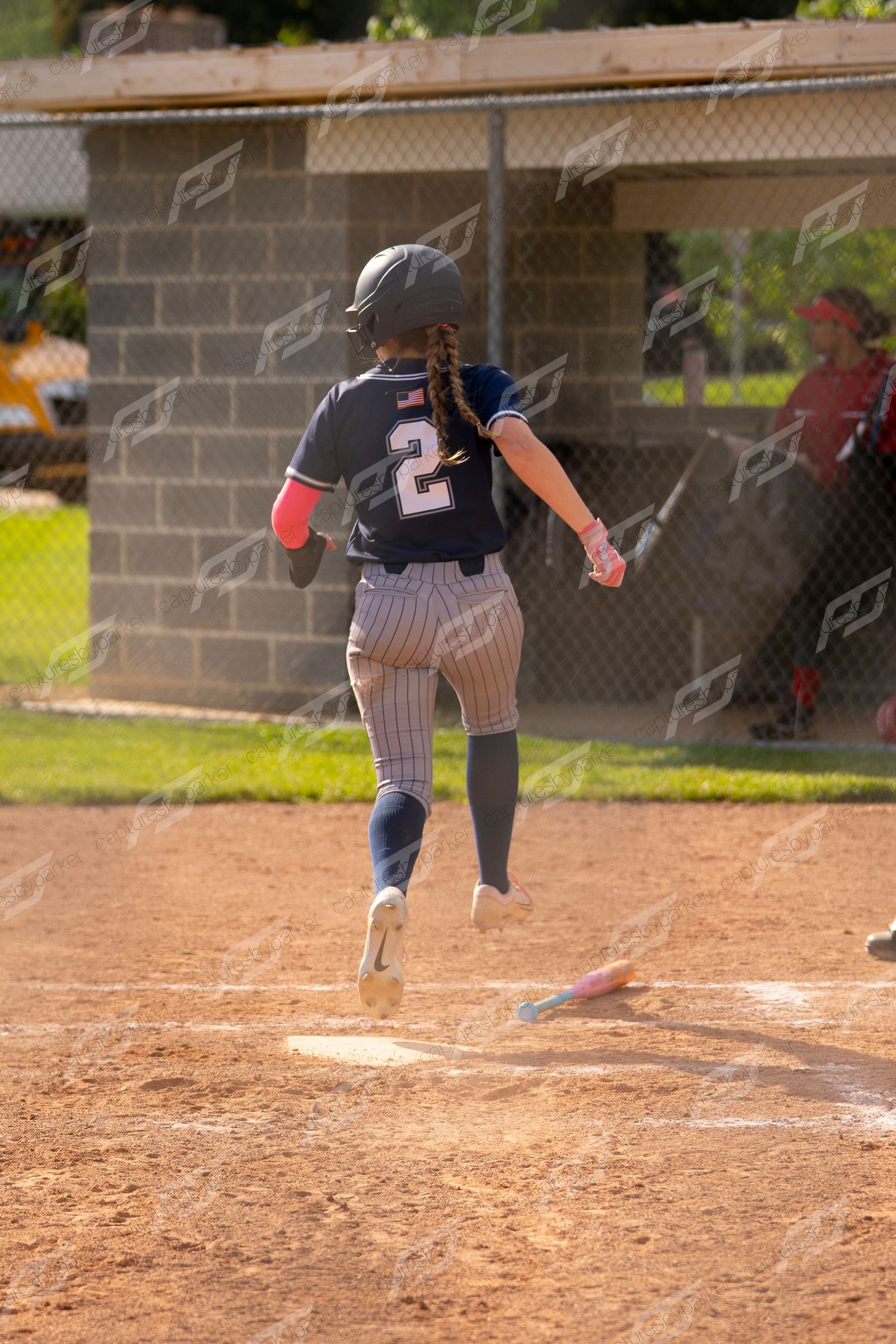 Softball player number 2 in navy pinstripe uniform sprints toward home plate during a game.