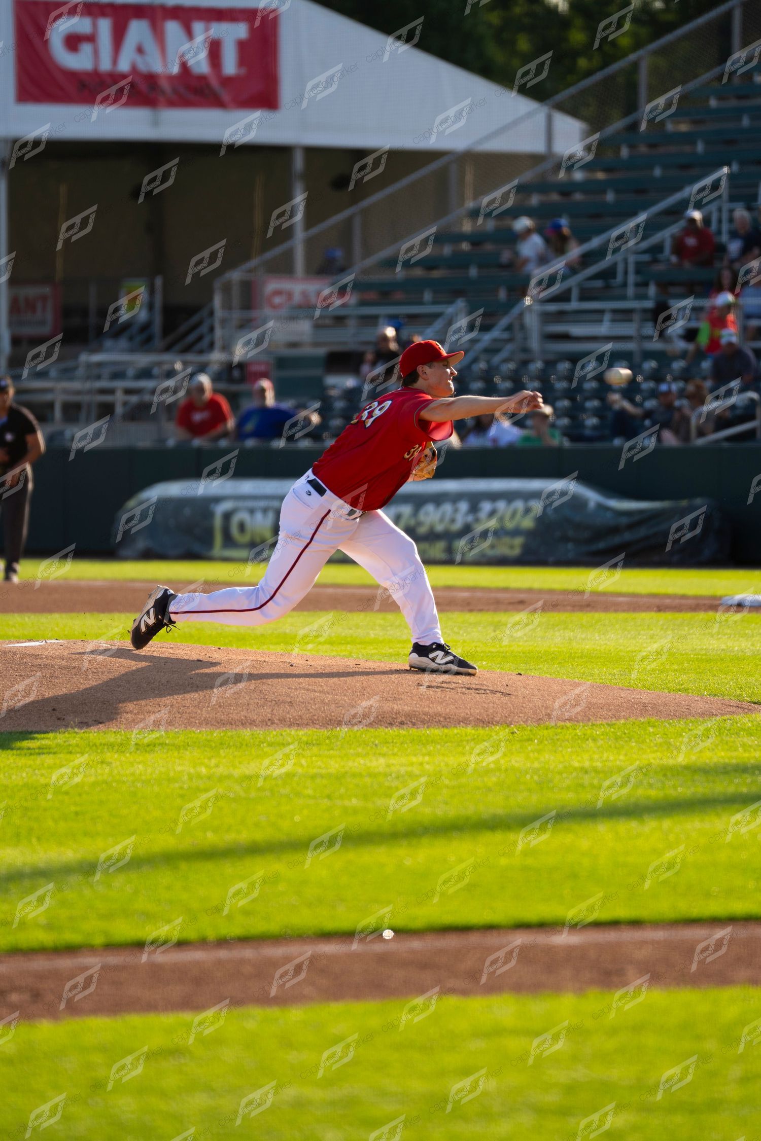 Baseball pitcher in red uniform delivering a pitch during a game with GIANT signage in background.