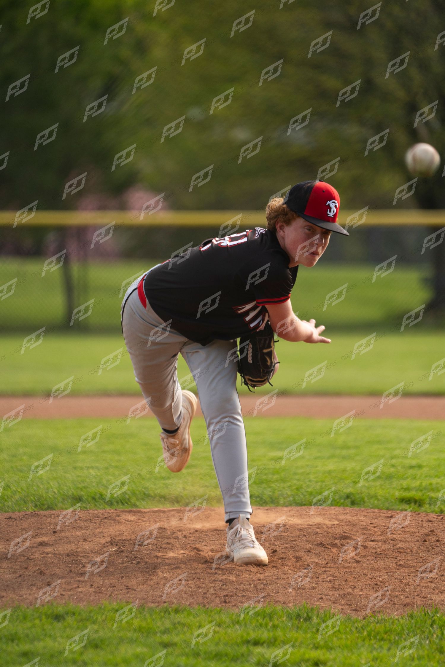 Hanna baseball pitcher in black and red uniform following through on a pitch delivery from the mound.