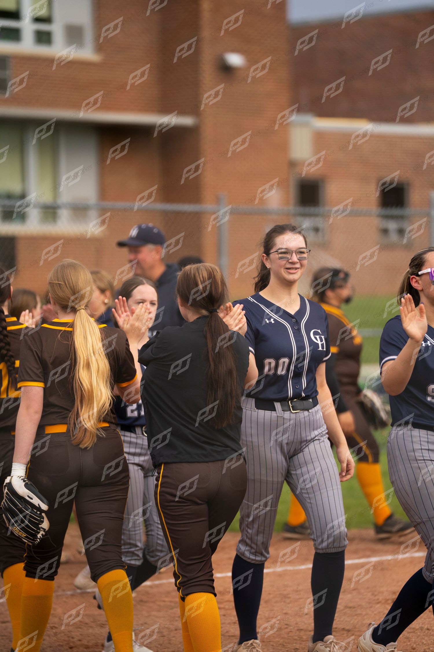Smiling softball player in navy uniform high-fives opponents in post-game handshake line.