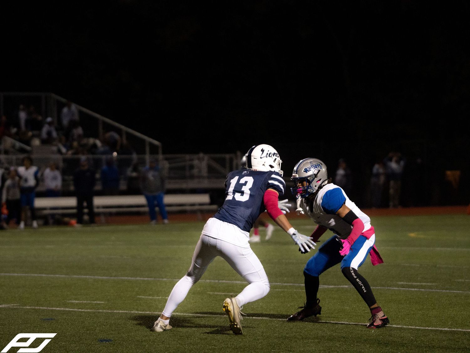 Camp Hill Lions player number 13 faces off against an opponent during a night football game.