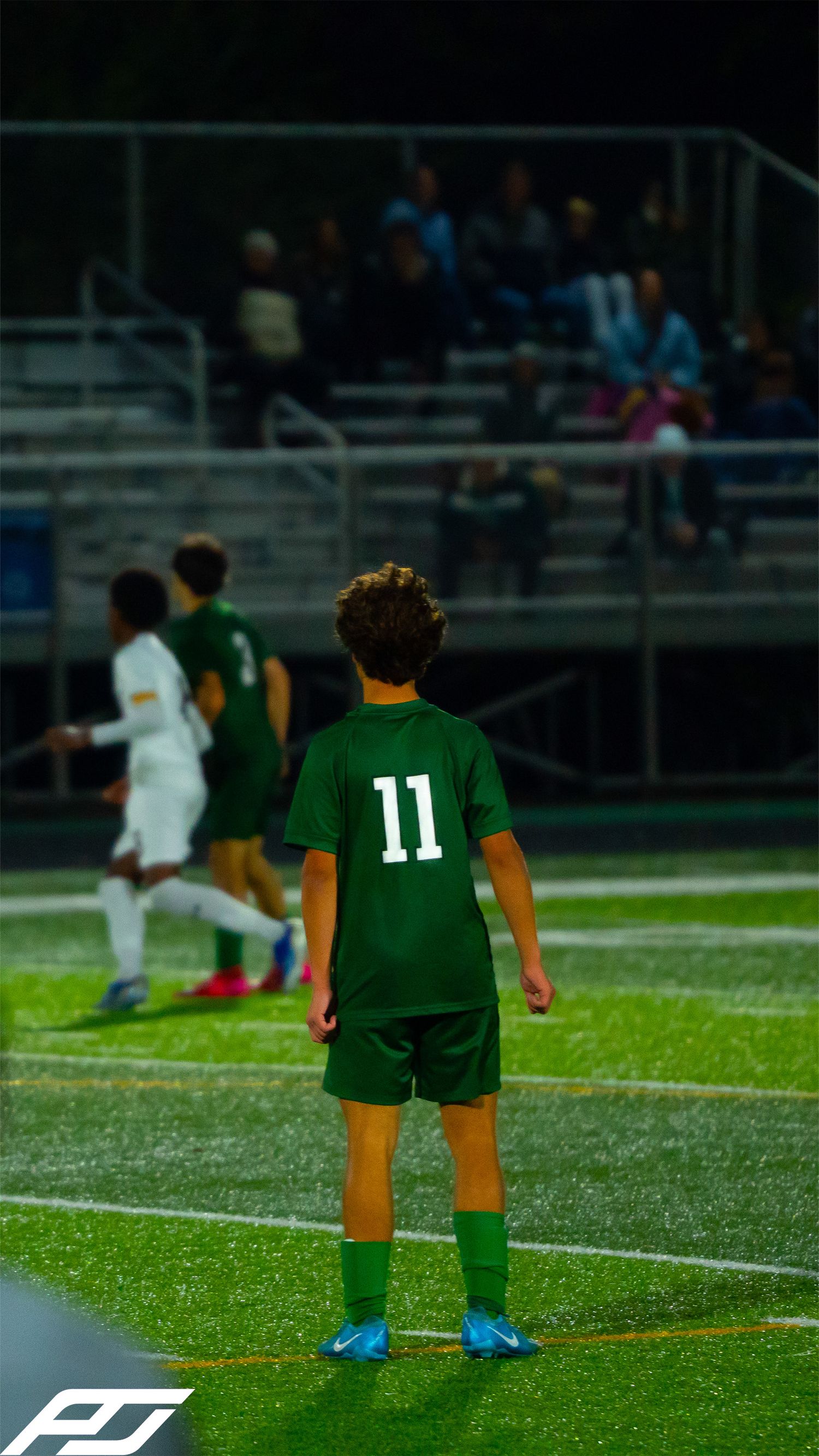 Trinity soccer player wearing green jersey number 11 stands on the turf field during a nighttime game.