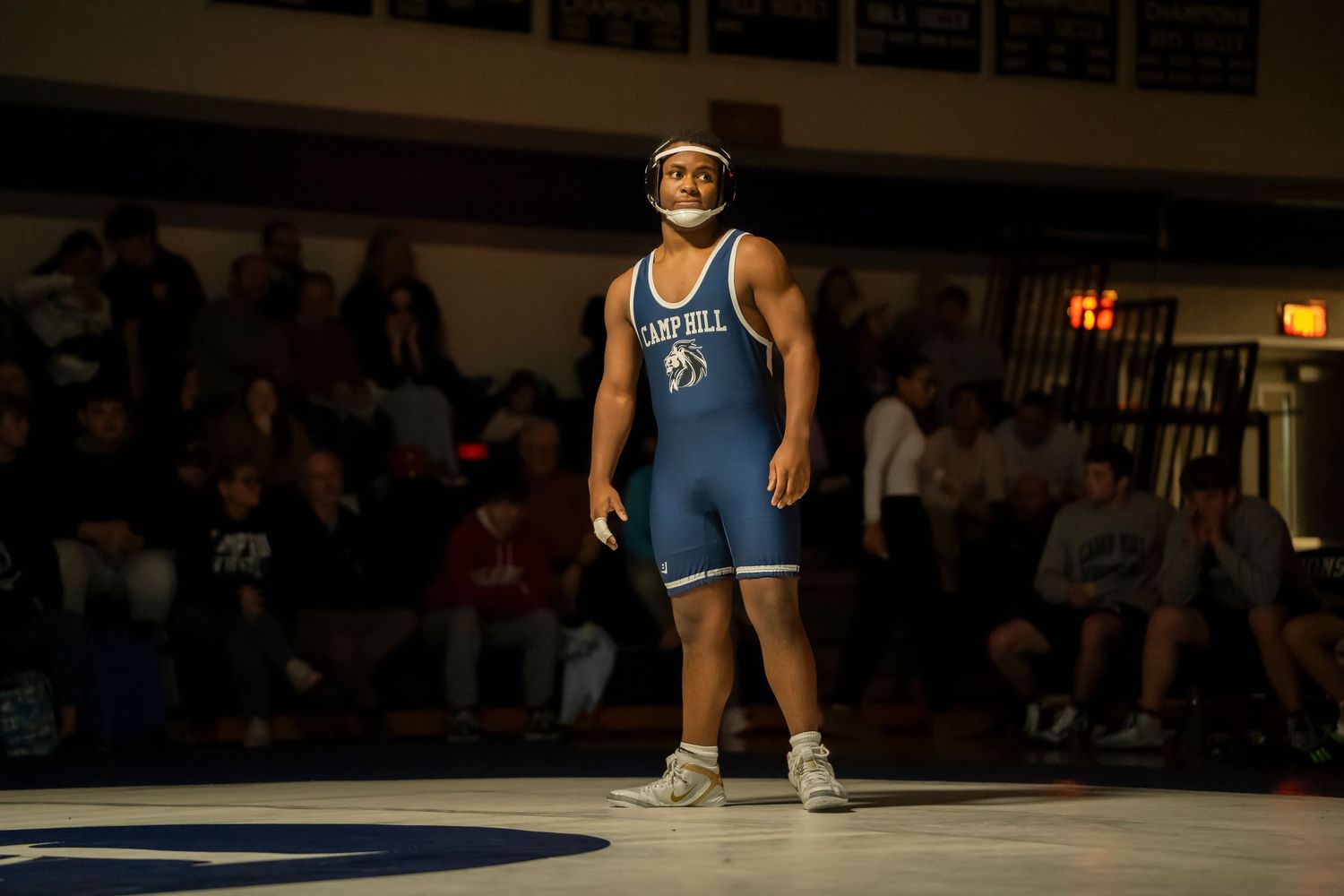 Campbell University wrestler stands confidently on the mat in a blue singlet before a match.