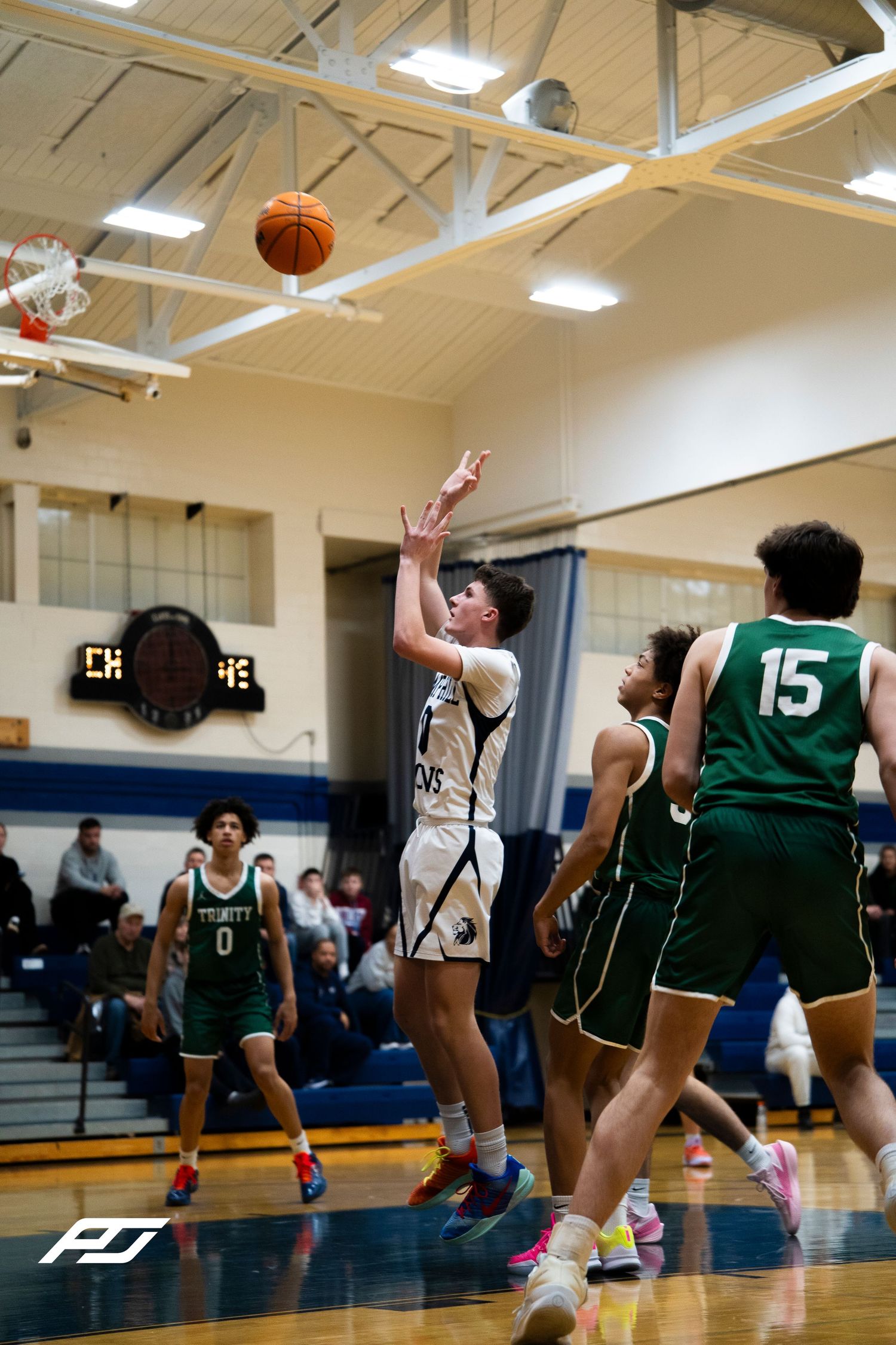 Camp Hill Lions player releases a jump shot over Trinity defenders #15 during a basketball game.