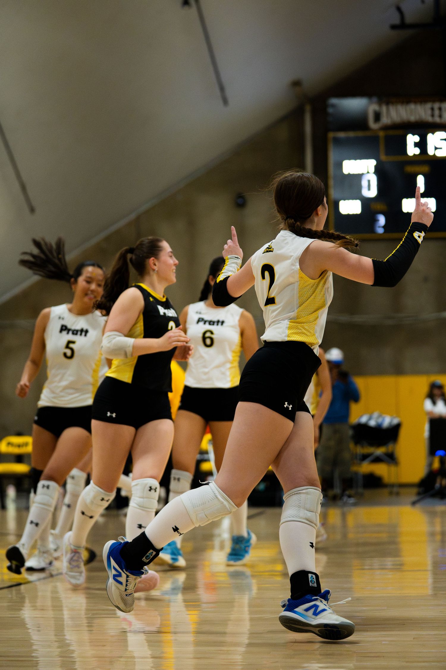 Pratt volleyball players in black and gold uniforms celebrate on court, with player number 2 giving a high five.