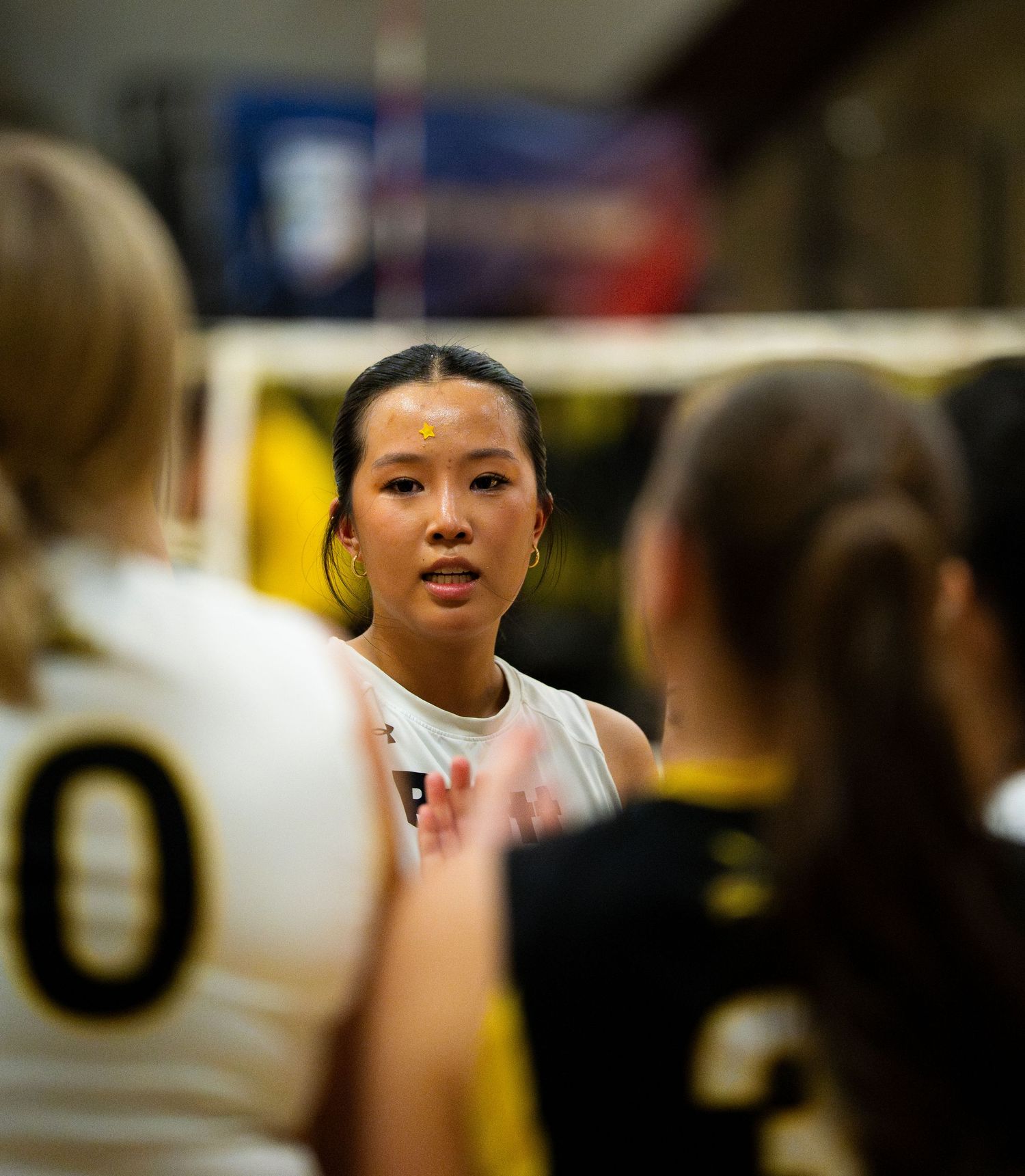 Female volleyball player in white jersey speaks to teammates in black and white uniforms near the net during a match.