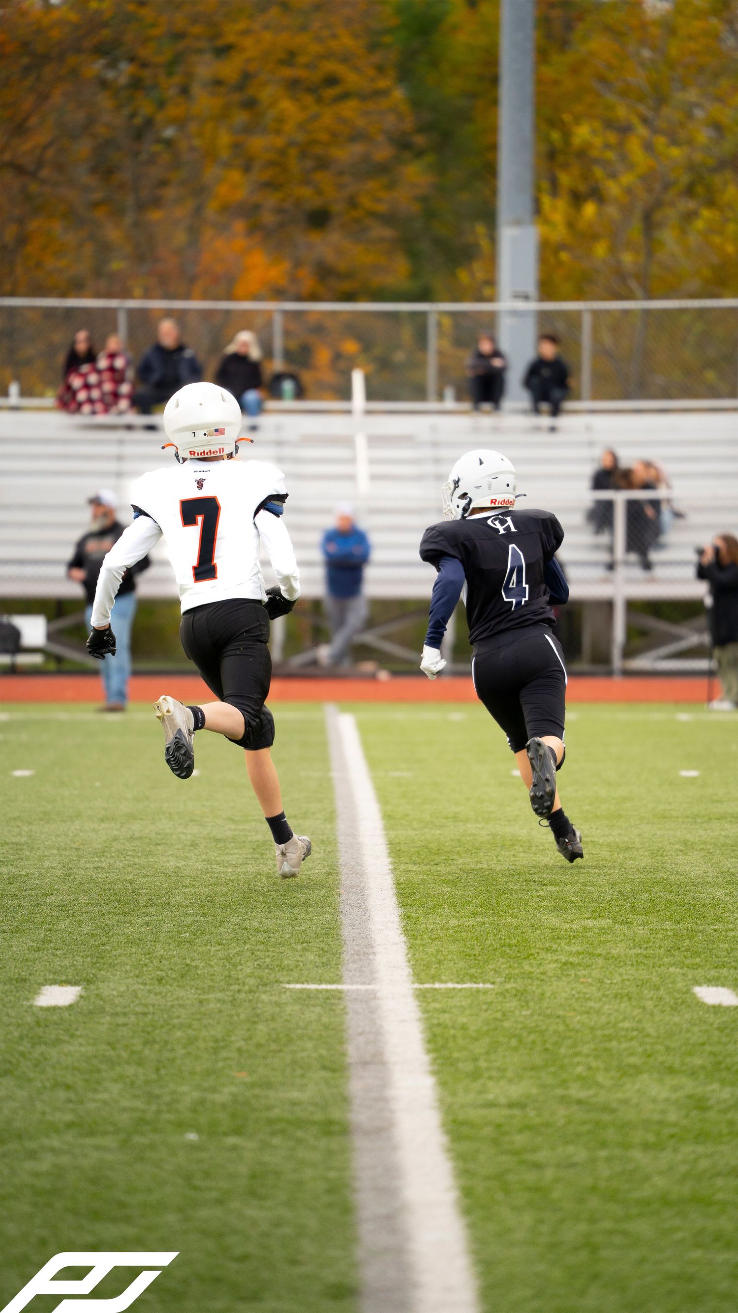 Two youth football players race downfield during a game on a green turf field.