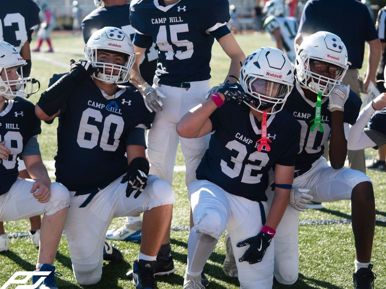 Young football players in Camp Hill jerseys celebrate on the field during a sunny game day.