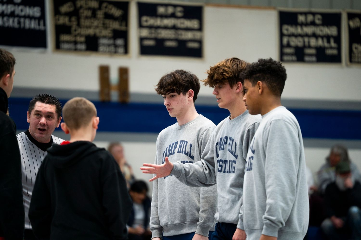 Camp Hill Wrestling team members confer with a coach near the wrestling mat.
