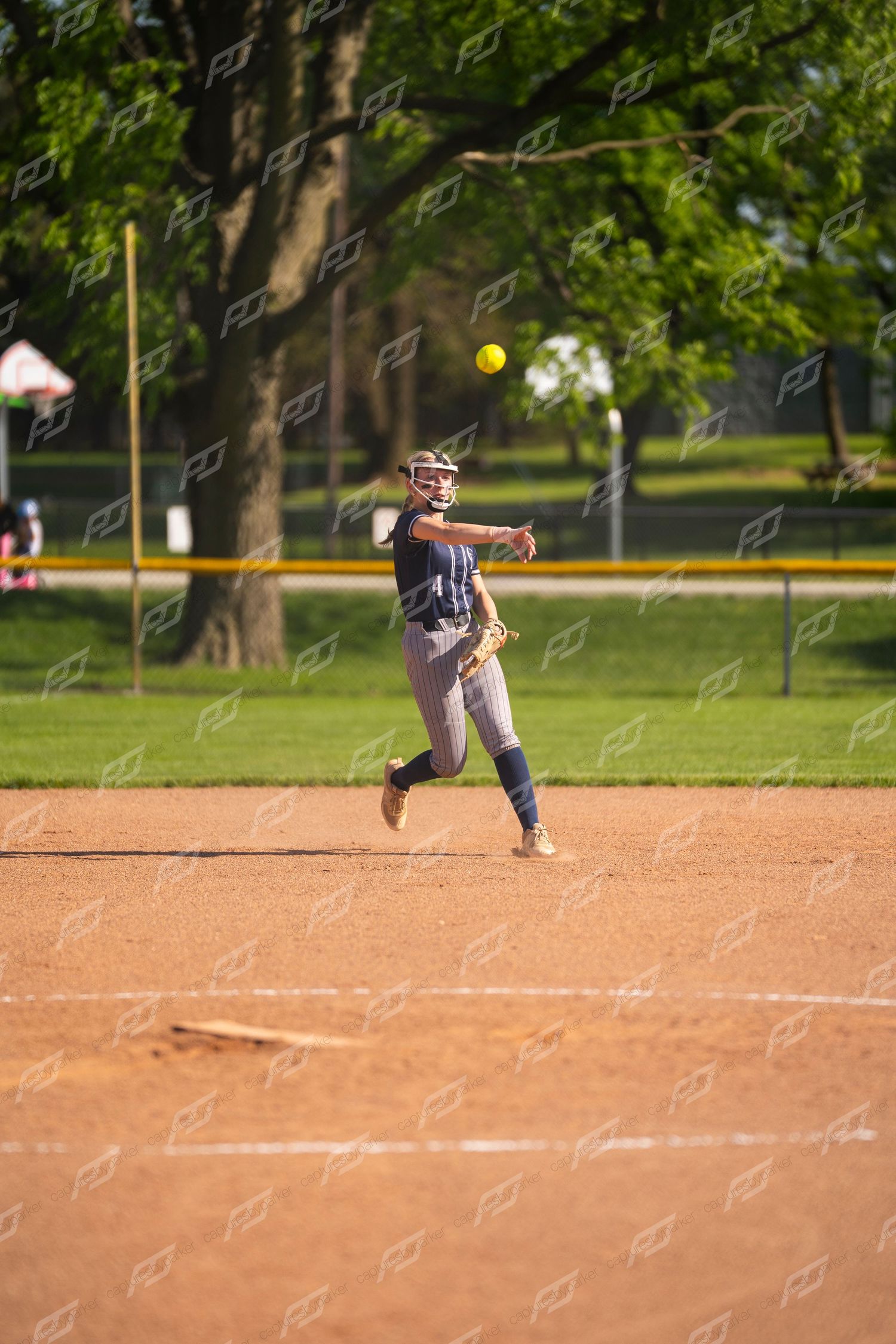 Female softball player throwing the ball across the infield dirt during an outdoor game.