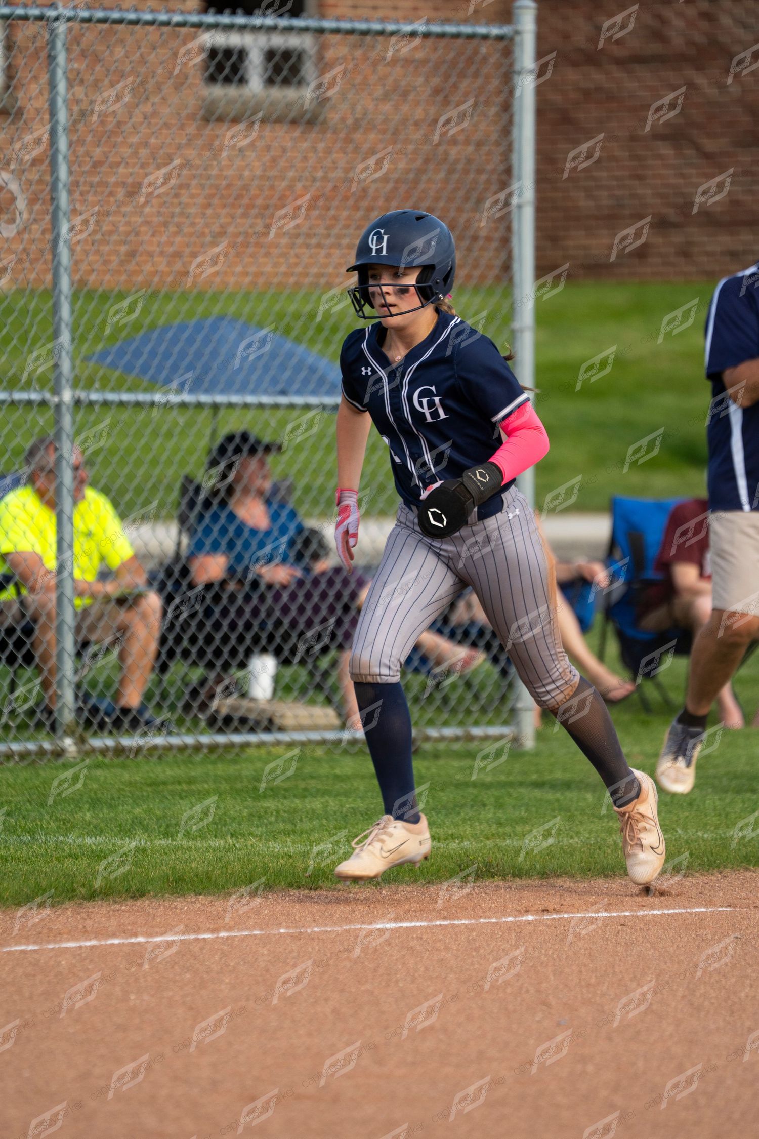 Female softball player in navy uniform runs bases during competitive game.