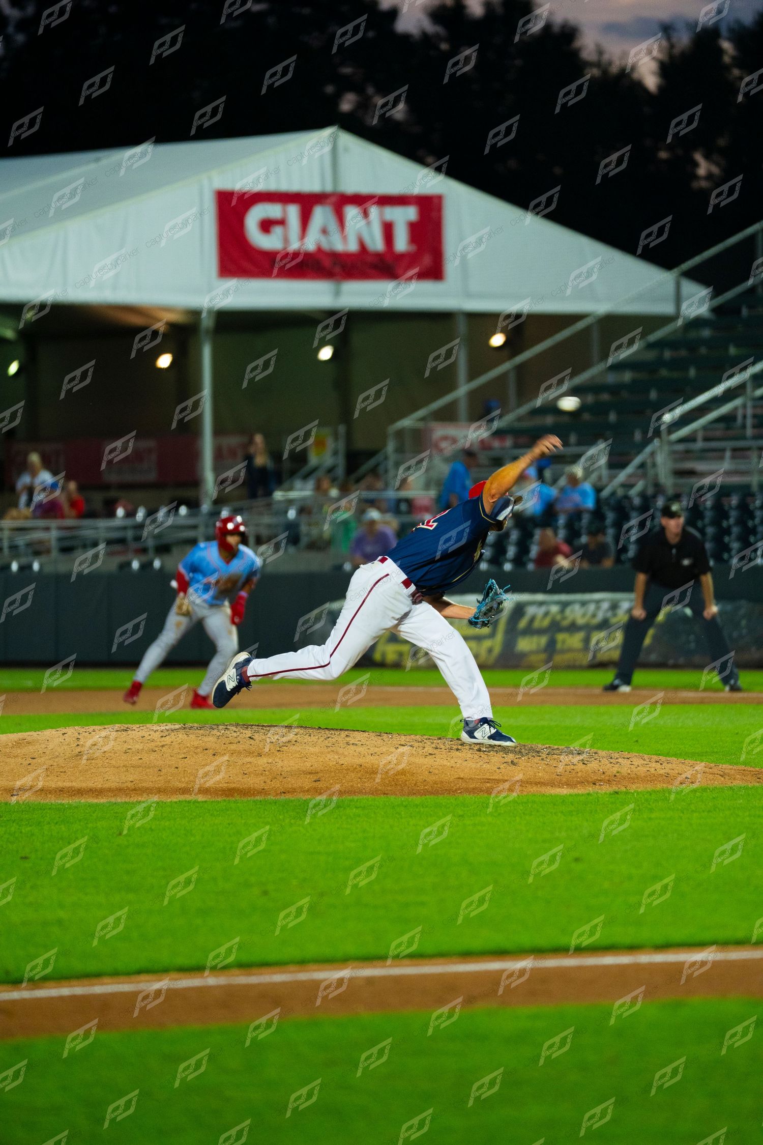 Baseball pitcher delivers a pitch from the mound during a night game with Giant banner visible.