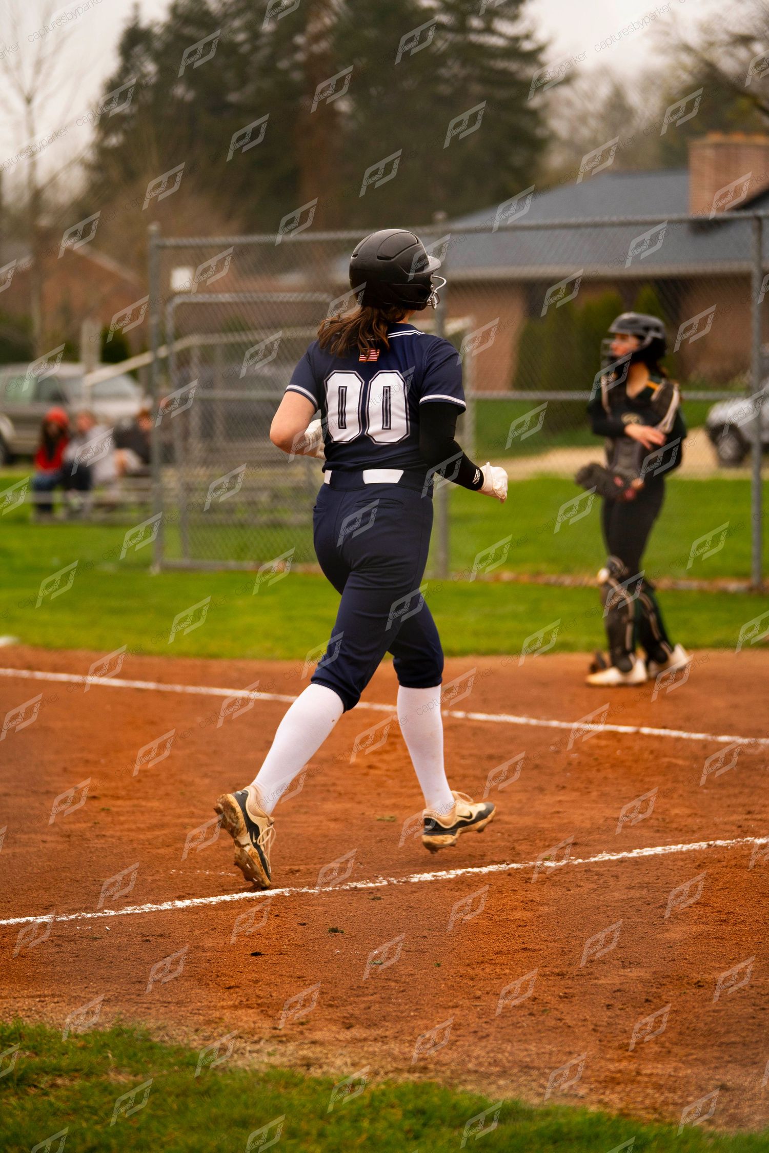 Softball player wearing number 00 runs toward home plate during a game.