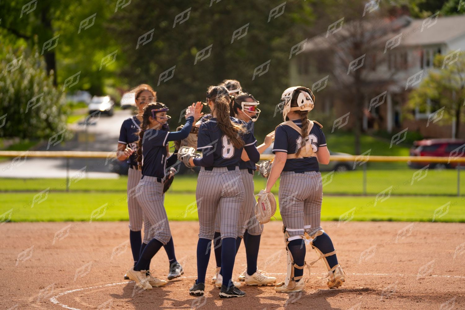 Female softball team huddles together celebrating on the field.