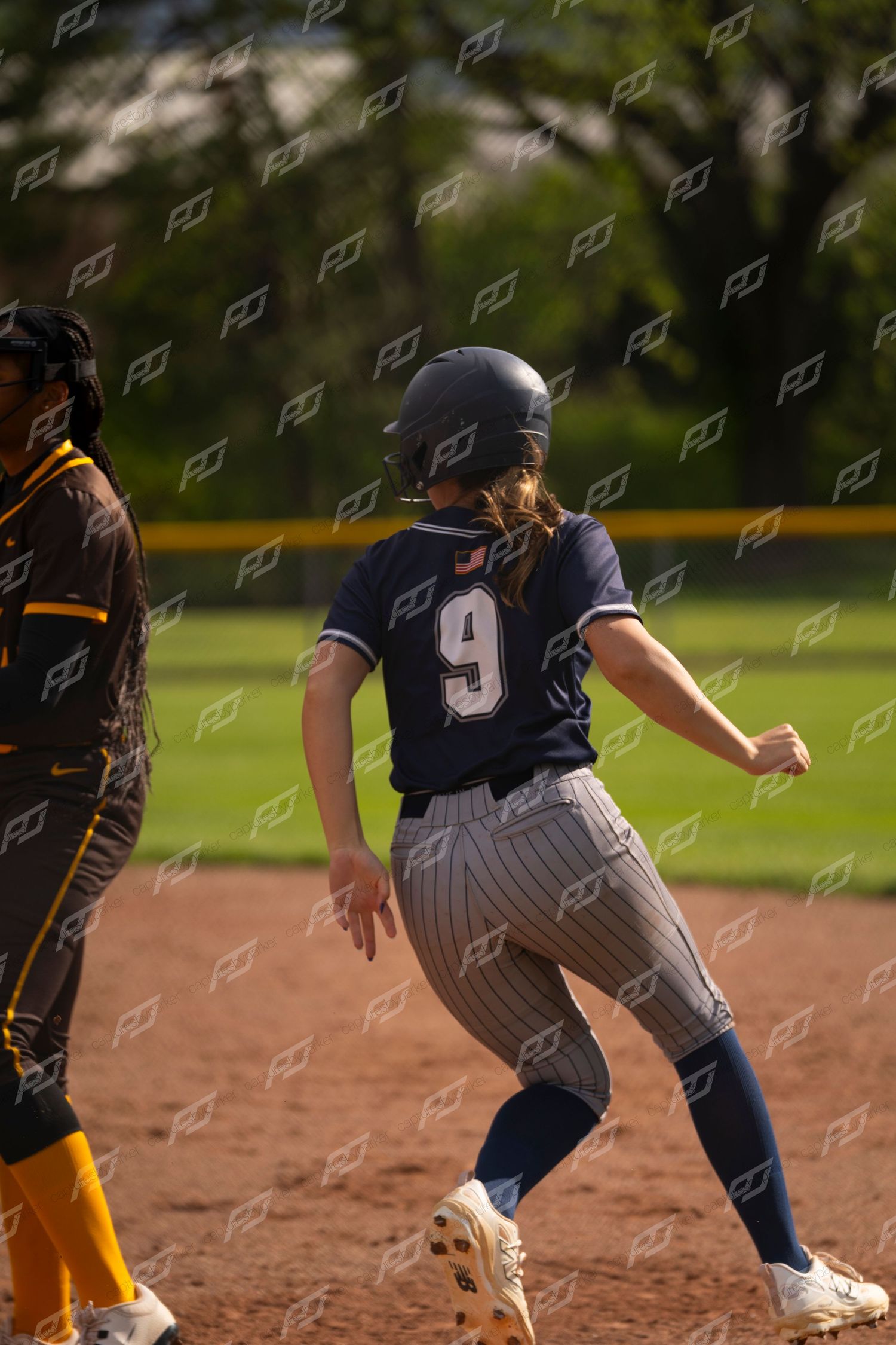 Female softball player wearing number 9 rounds a base during a softball game.