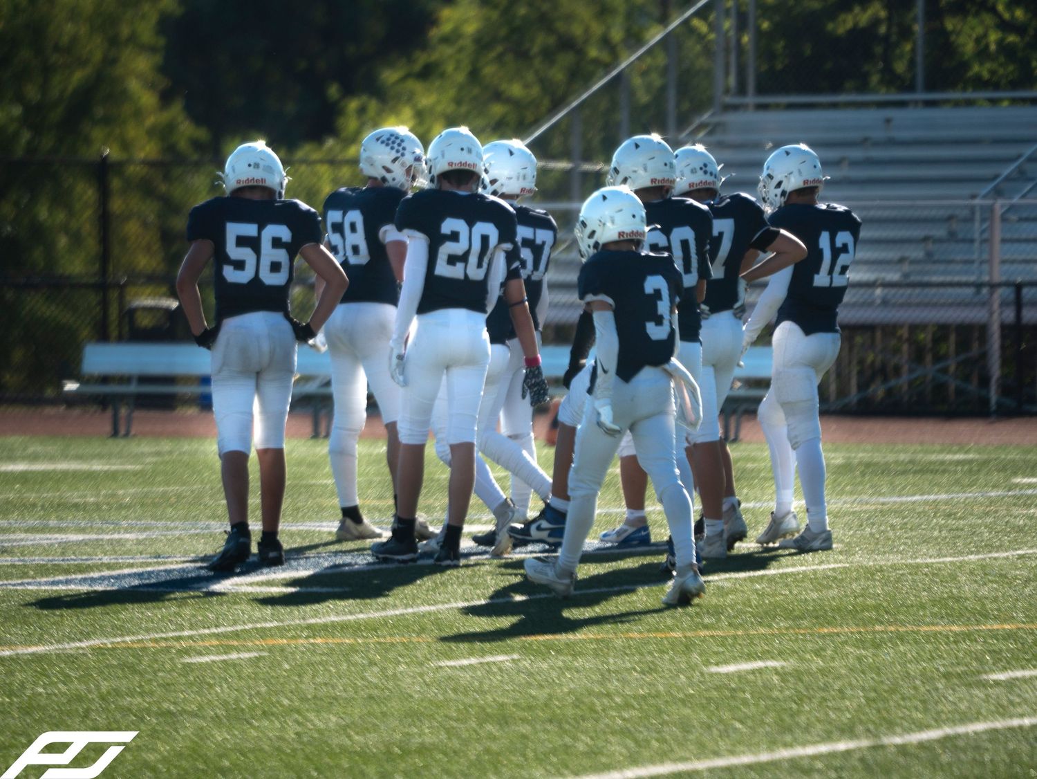 Camp Hill football team huddles together on green field wearing navy and white uniforms.