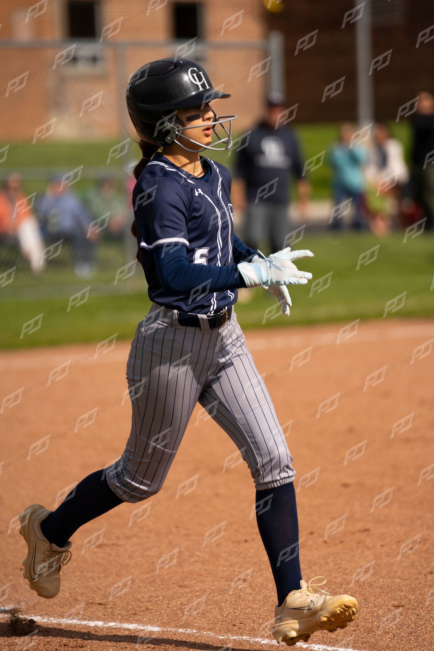 Female softball player runs bases wearing helmet and batting gloves.