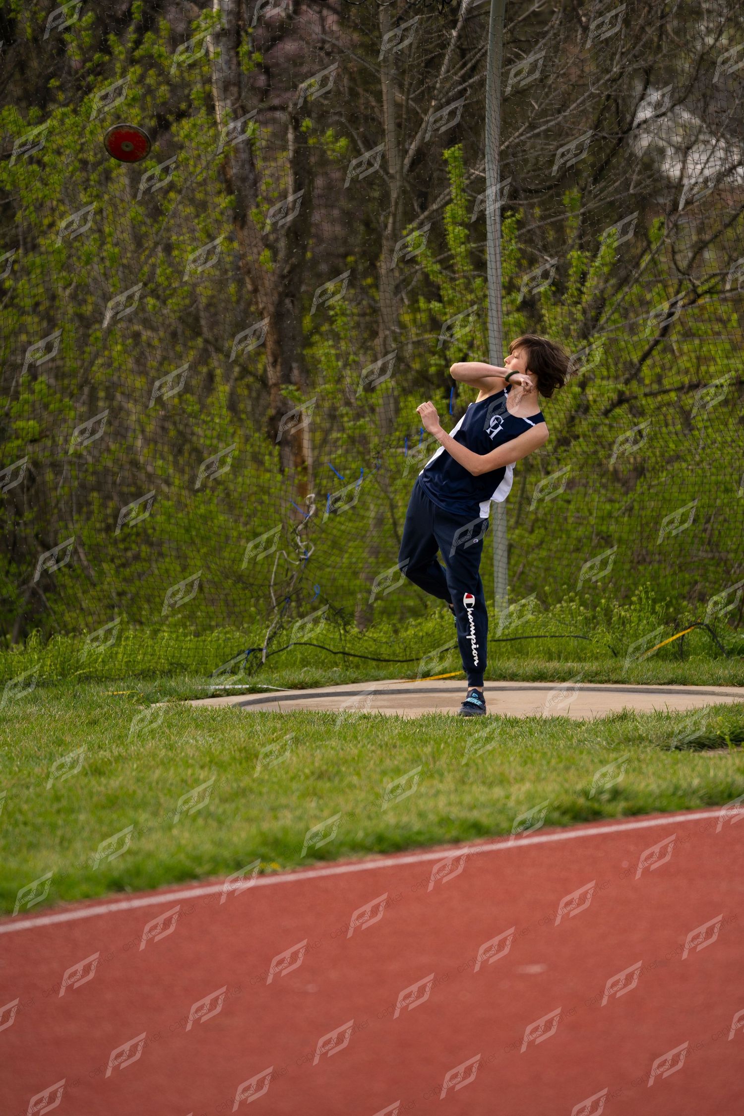 Young athlete in navy uniform throws a discus during an outdoor track and field event.