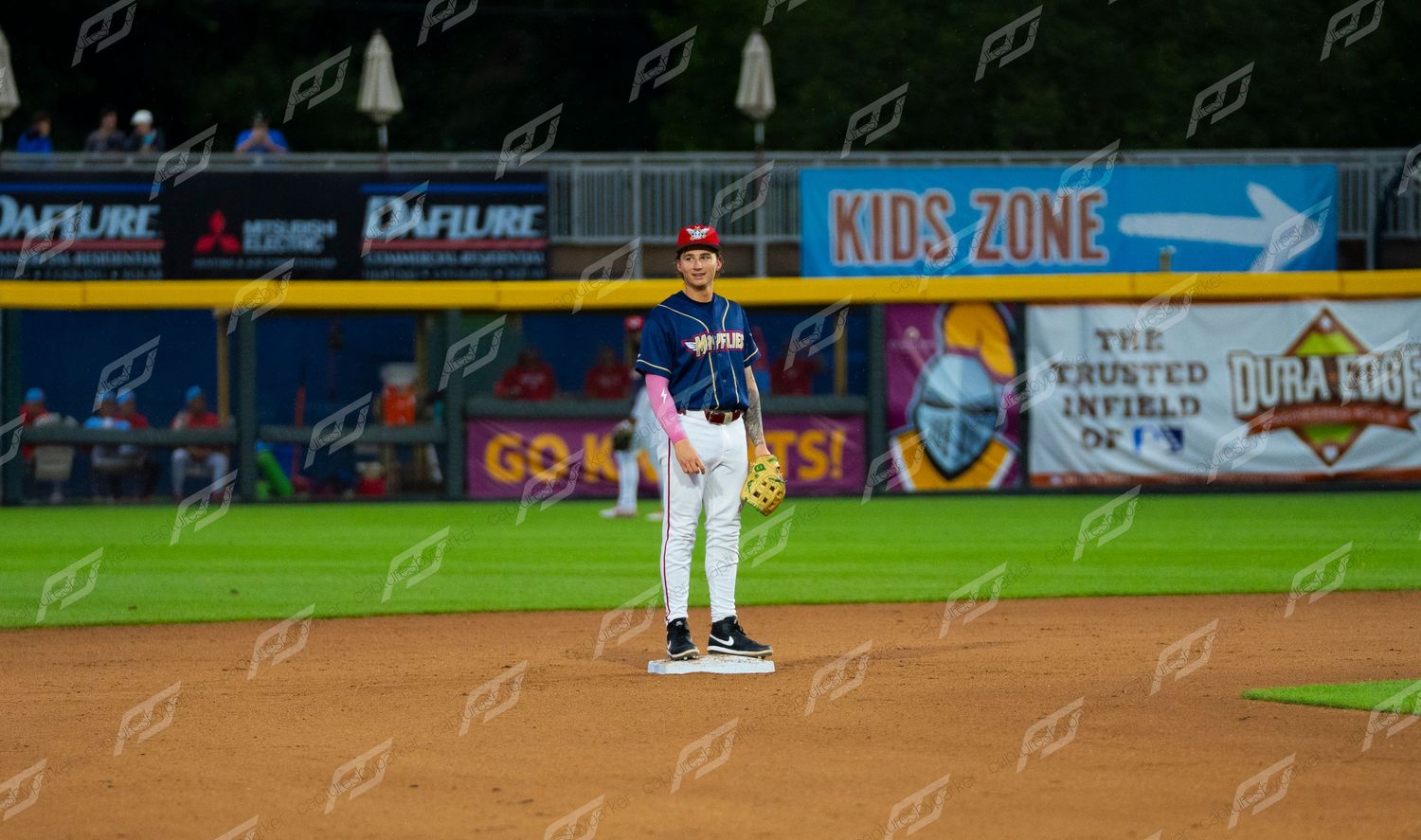 Baseball player stands at second base during a night game with Kids Zone sign visible in background.