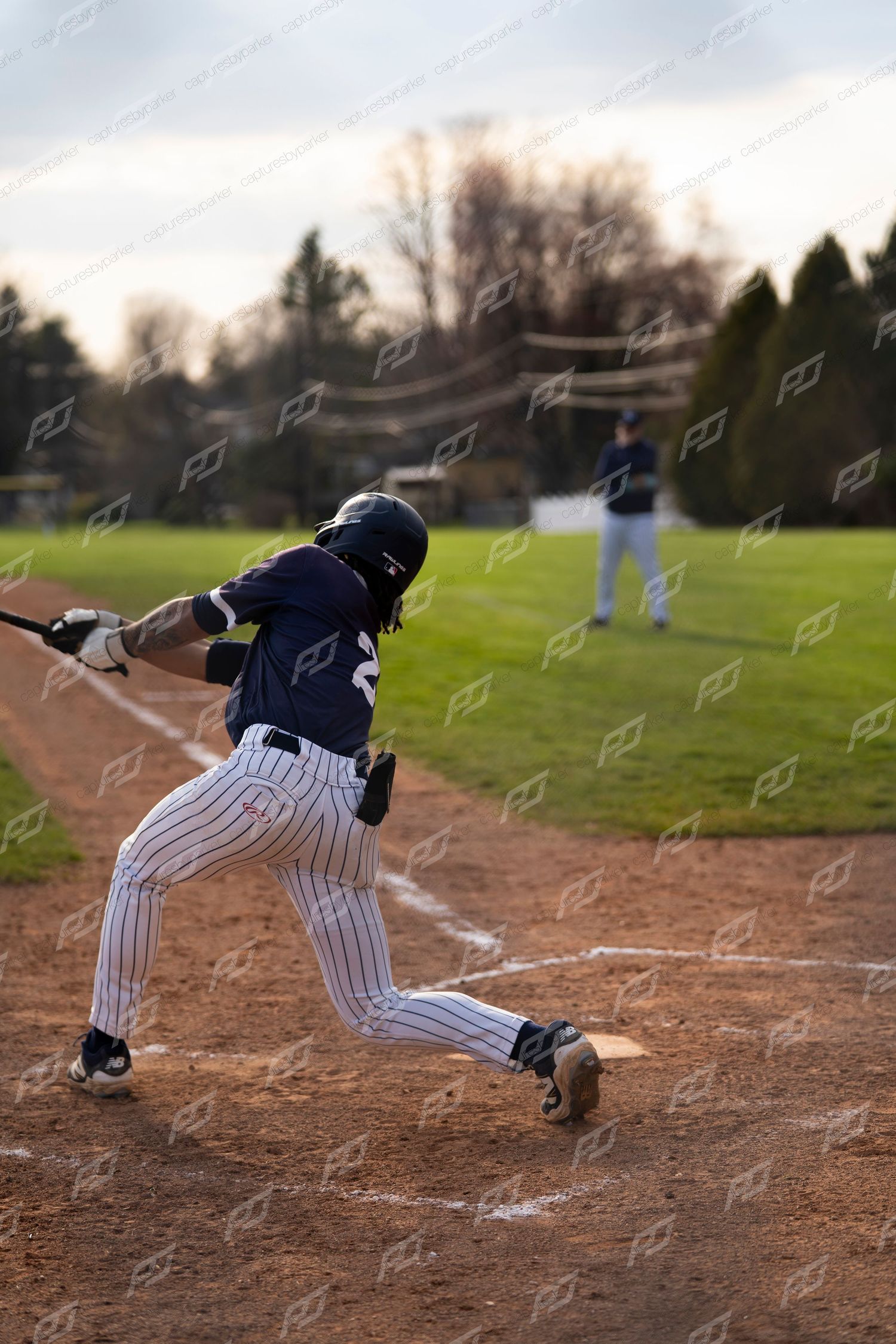 Baseball batter swings at a pitch during an outdoor game with a fielder in background.