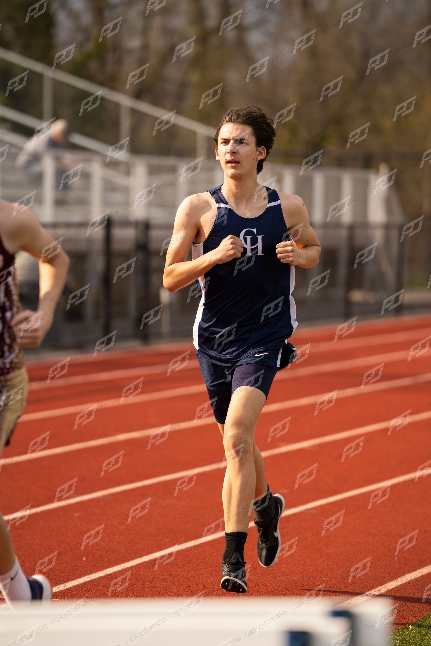 Male CH track athlete in navy singlet running on red track during competition.