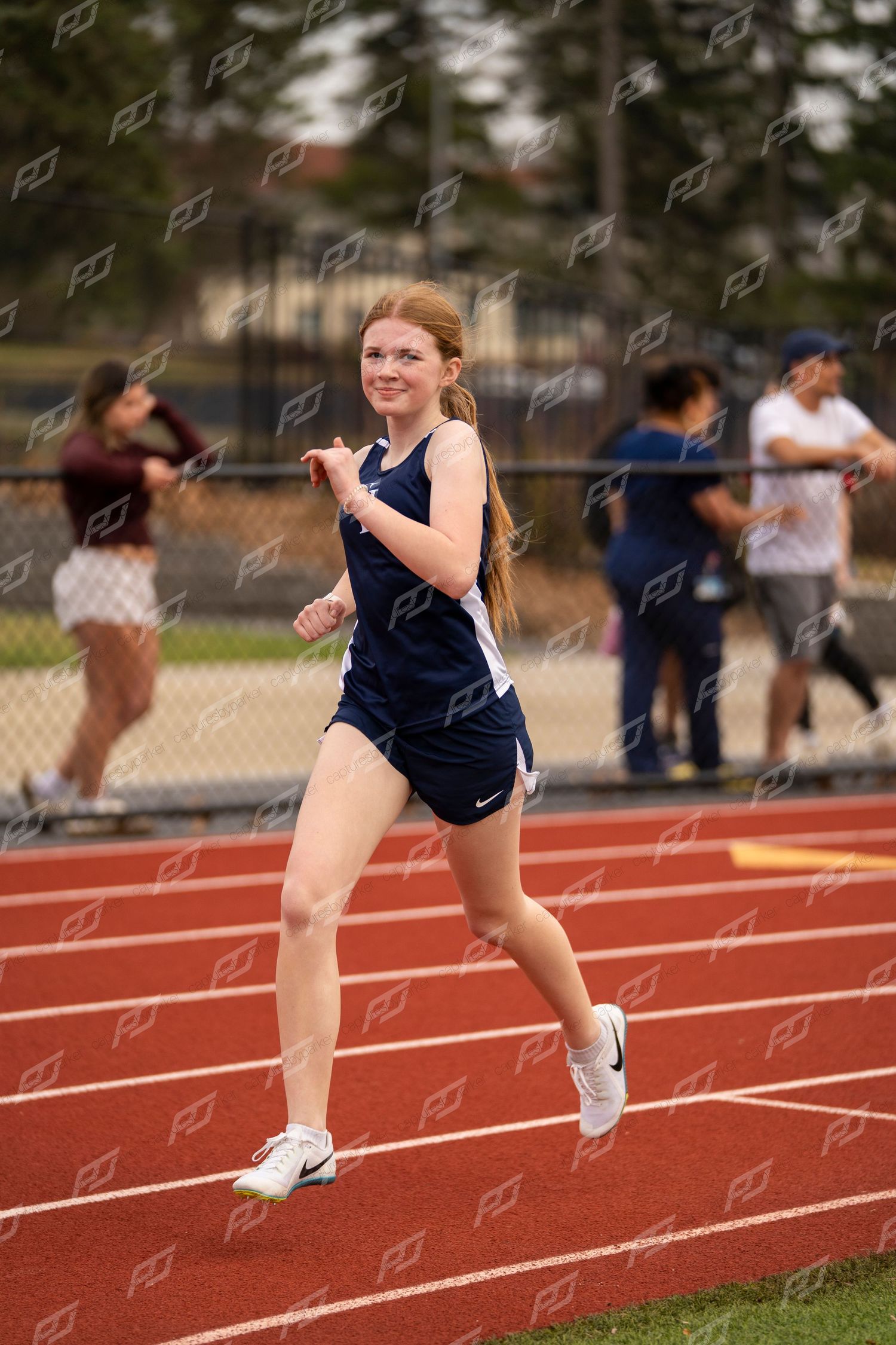 Female track athlete with red hair runs on red track during meet.