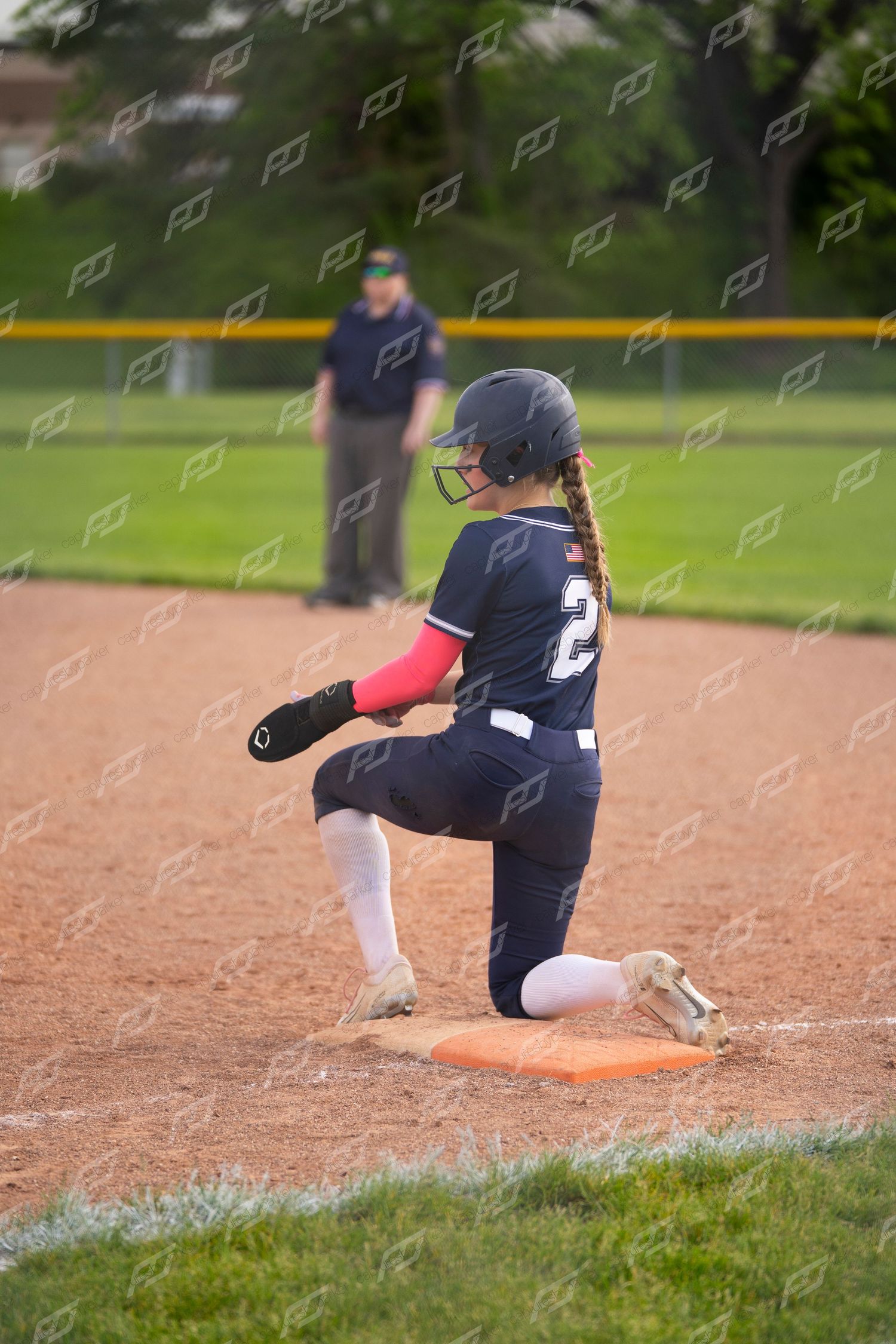 A softball player in navy uniform slides into an orange base during an evening game.